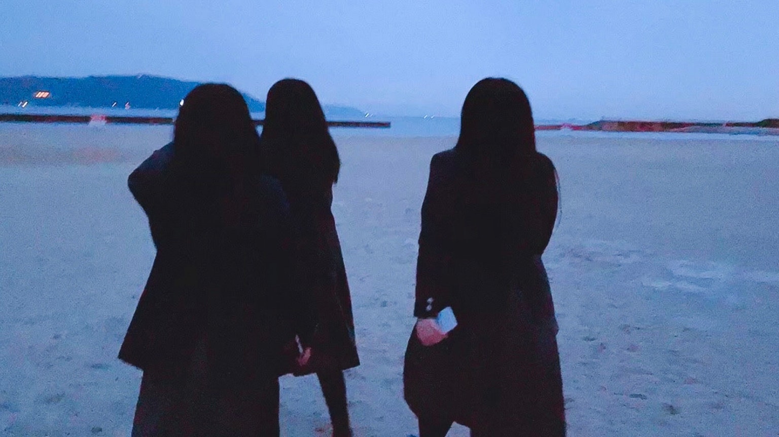 Drei Frauen in schwarzer Kleidung stehen am Strand in der Dämmerung