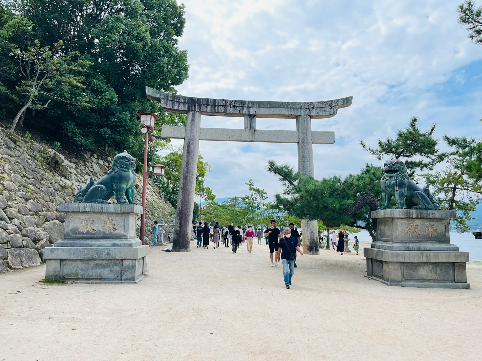 Ingresso di un santuario con un torii e statue di leoni guardiani molti visitatori presenti