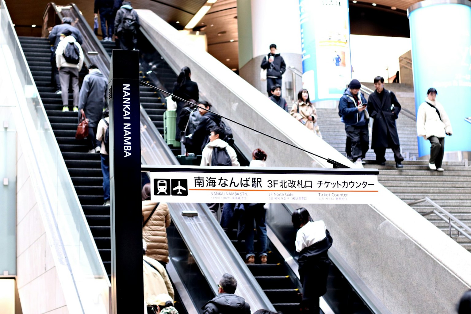 Interior view of a station with many people using the escalator