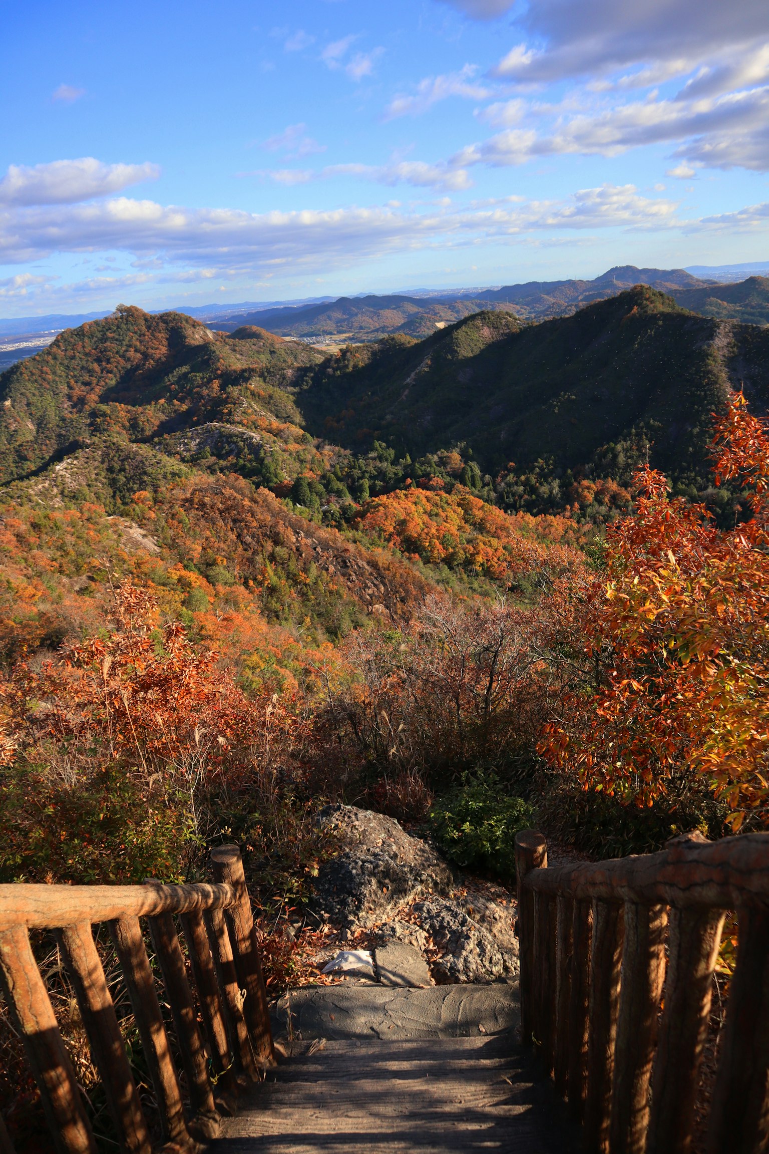 Scenic view of a mountain path surrounded by autumn foliage blue sky and clouds wooden handrail staircase