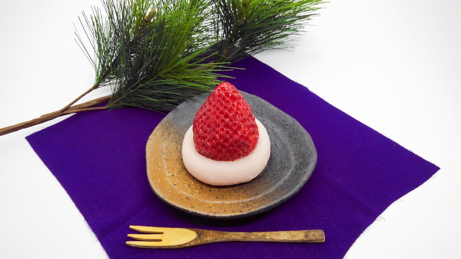Một món tráng miệng Nhật Bản với bánh mochi được trang trí giống như dâu tây trên đĩa tối màu với nĩa vàng và vải màu tím