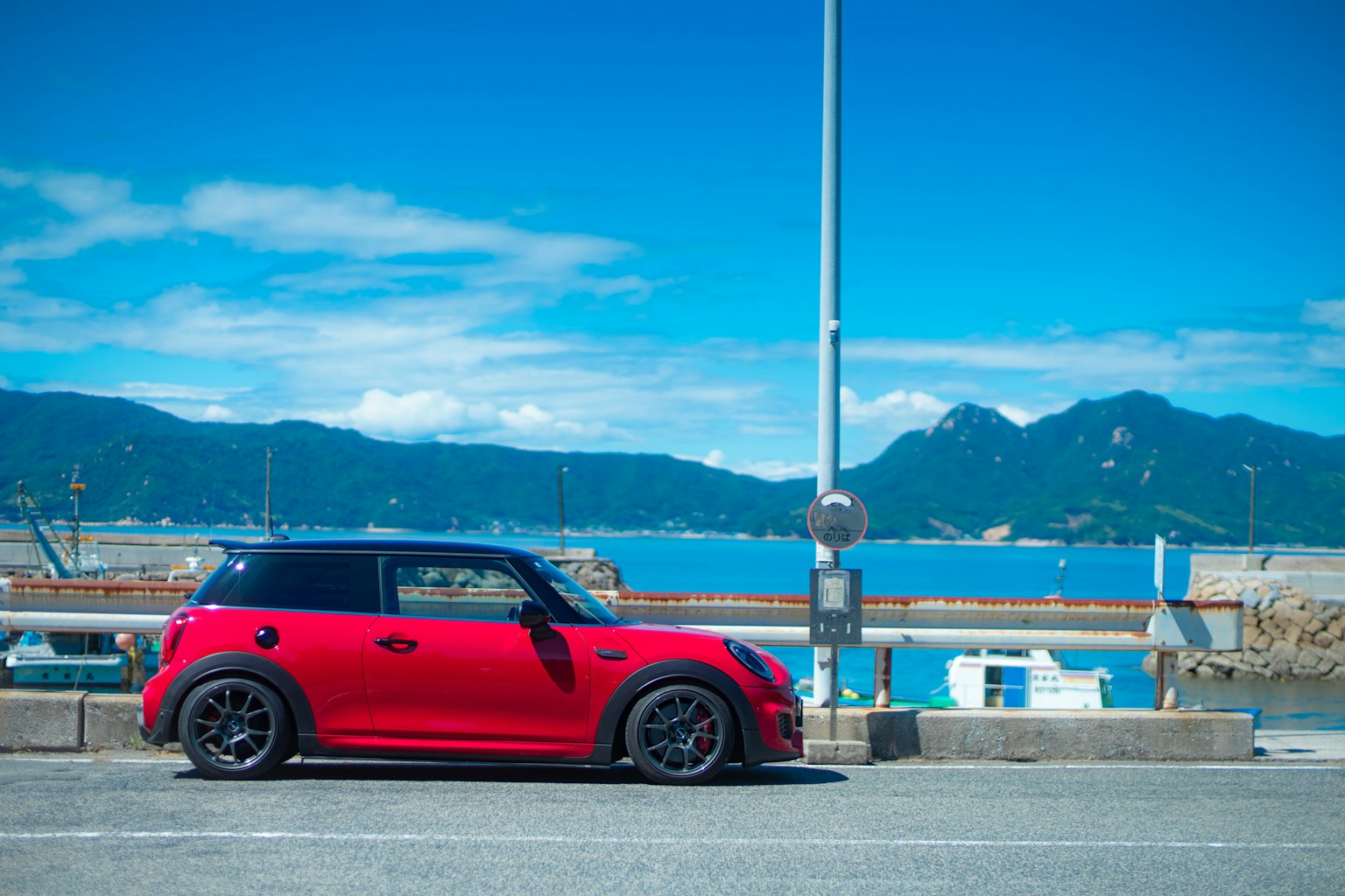 Mini Cooper rouge garée au bord de la mer avec un ciel bleu et des montagnes en arrière-plan