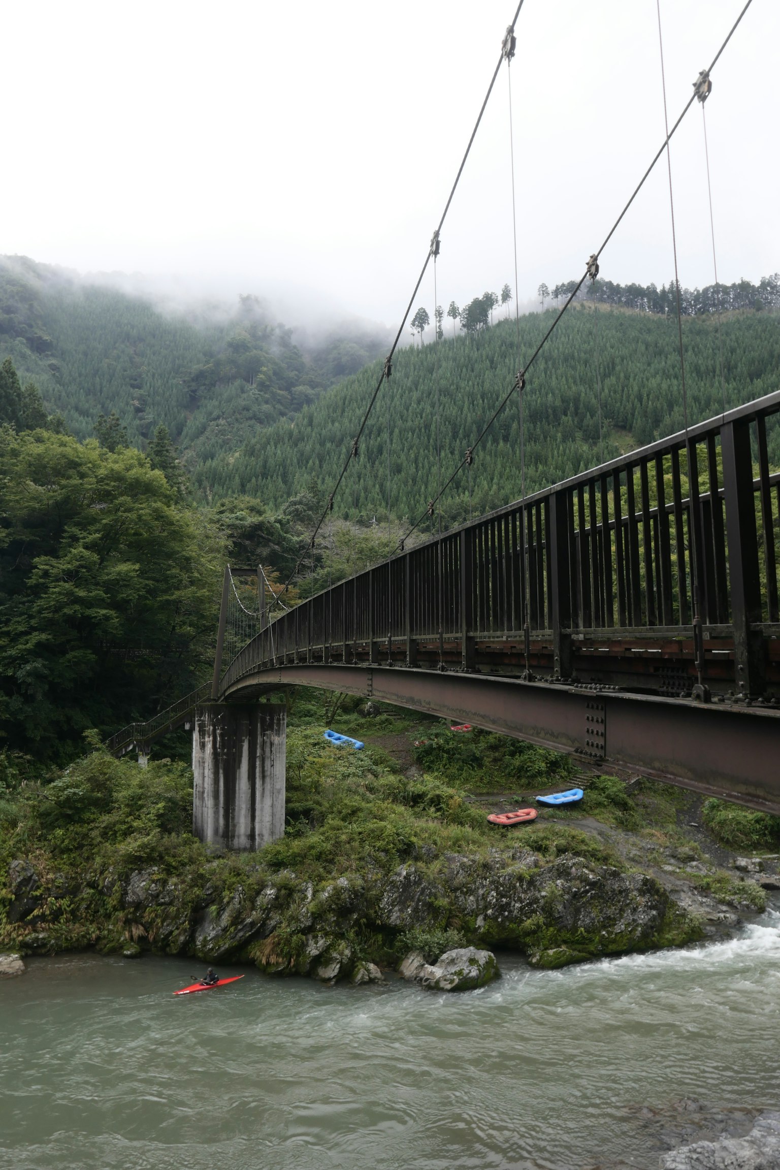 Ponte sospeso su un fiume circondato da montagne nebbiose e vegetazione