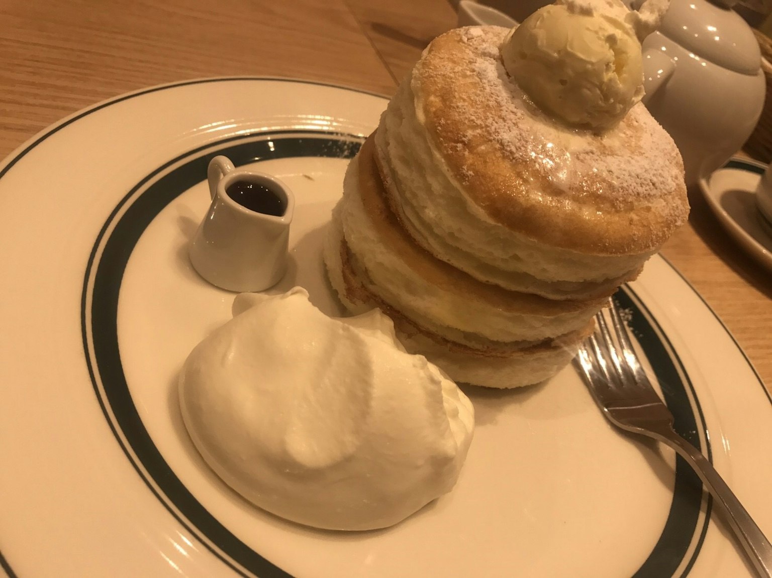 Pancake soffici impilati con burro sopra serviti con panna montata e un piccolo bicchiere di marmellata