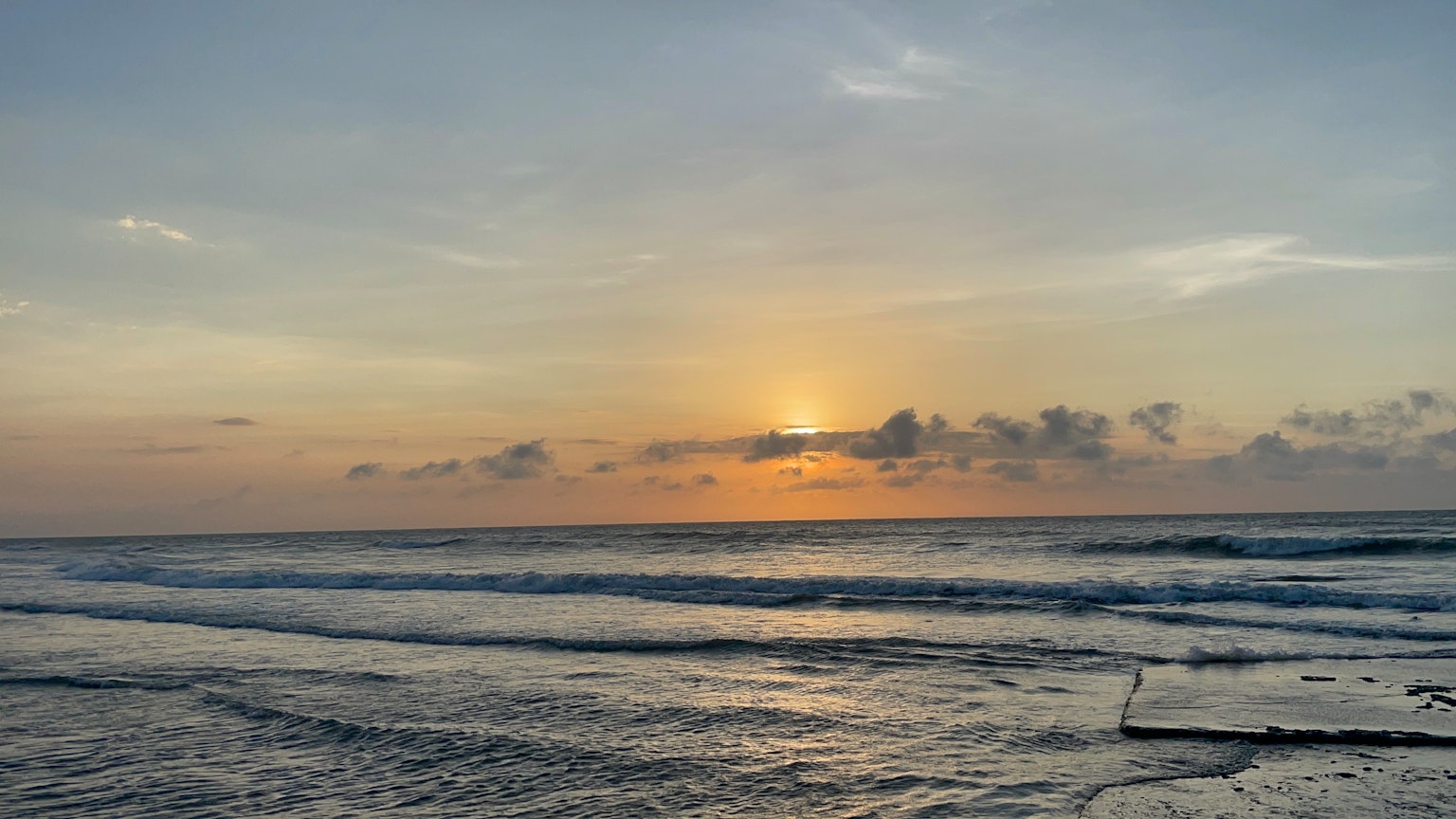 Küstenuntergang mit sanften Wellen und buntem Himmel