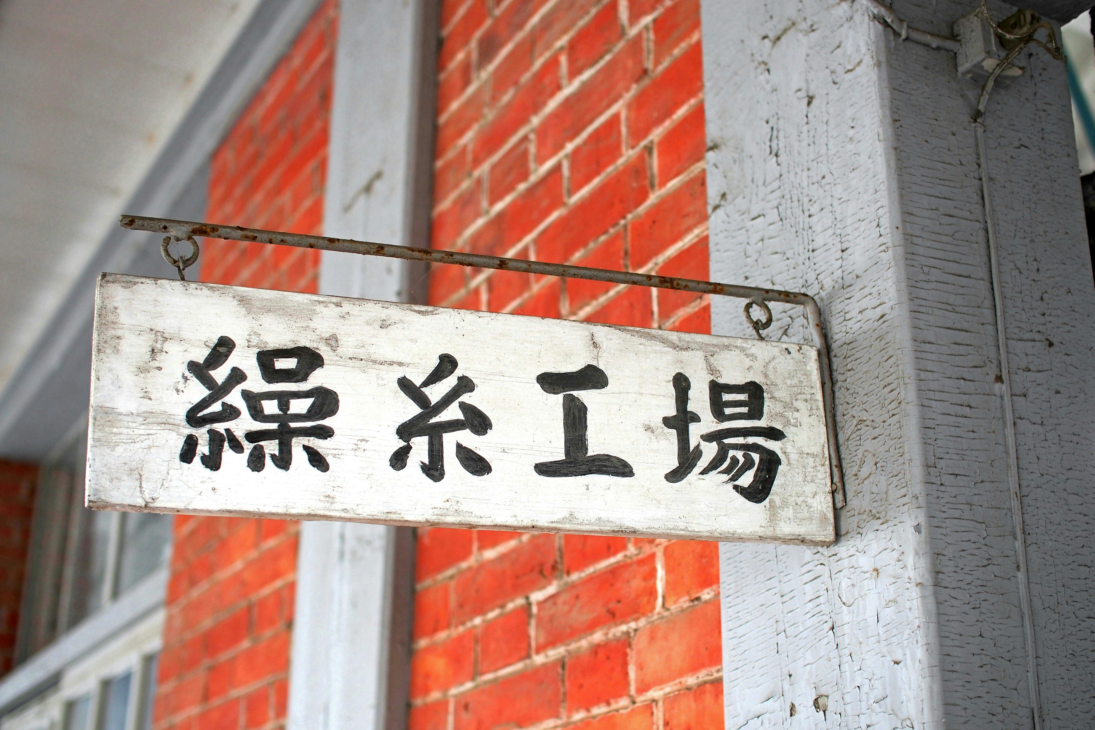 赤いレンガ壁の軒先に掛かった「綠糸工場」の看板