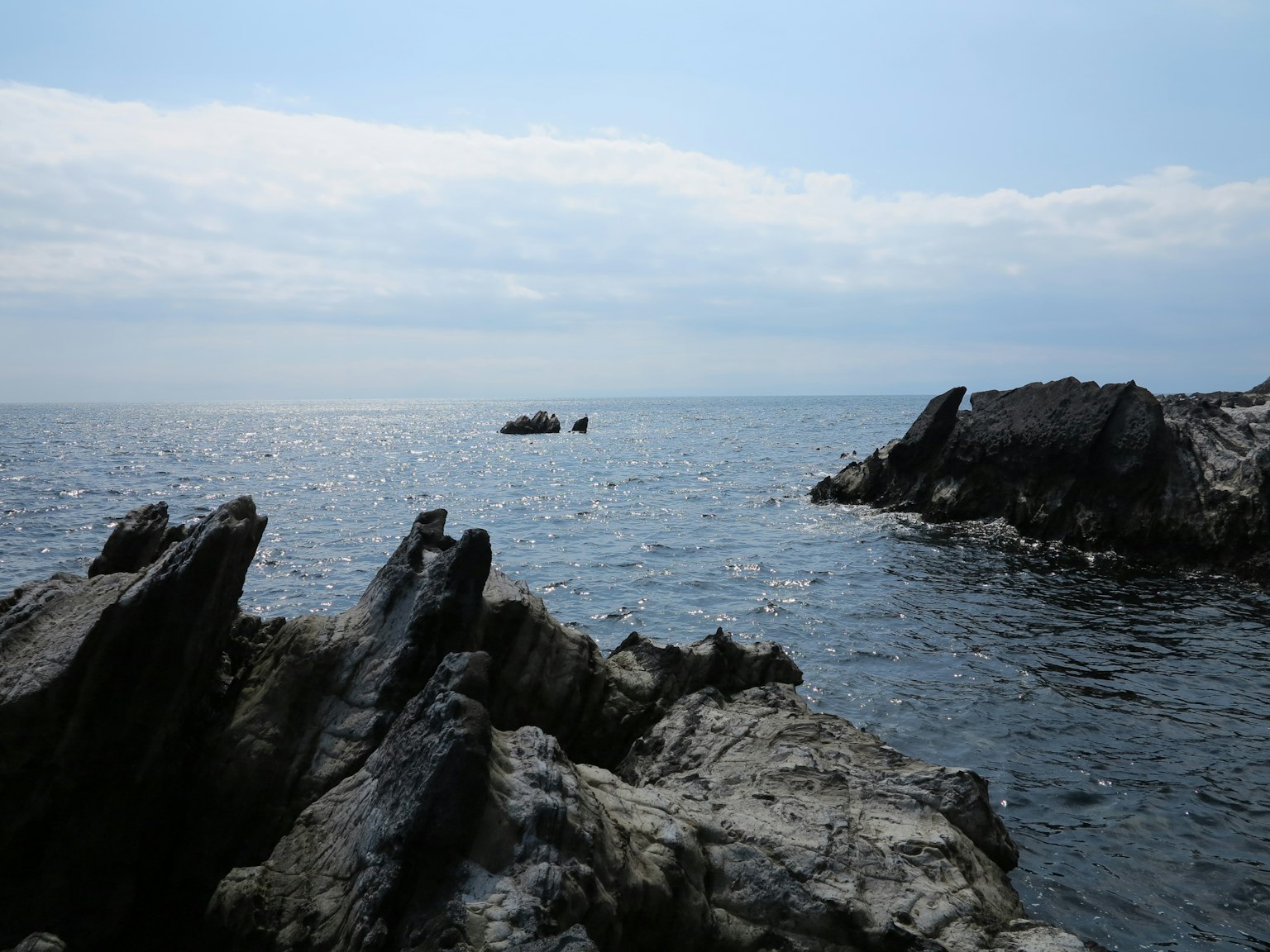 Pemandangan pantai dengan tebing berbatu, laut tenang, langit biru