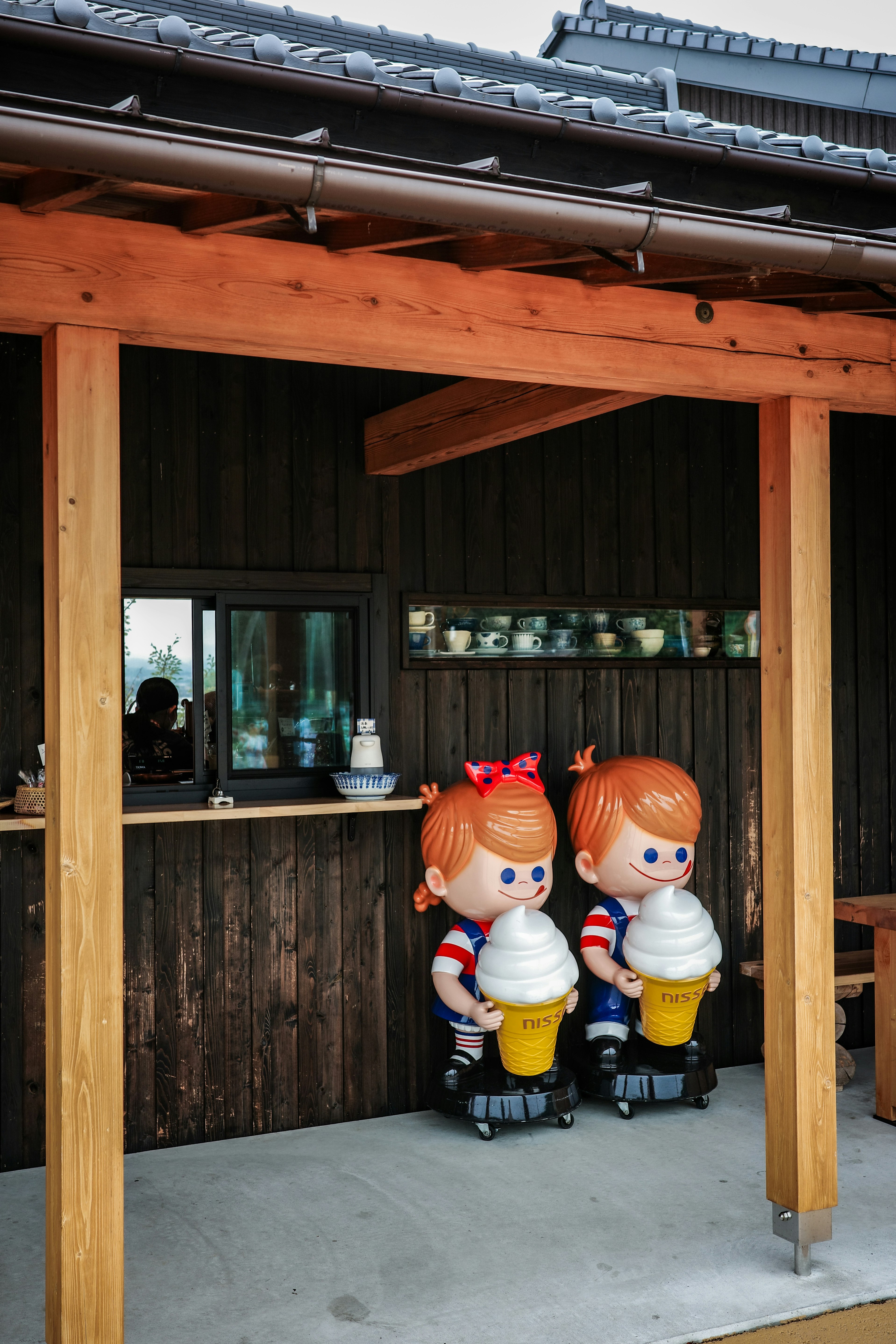 di bawah atap kayu ada deretan boneka figur dan rak peralatan makan
