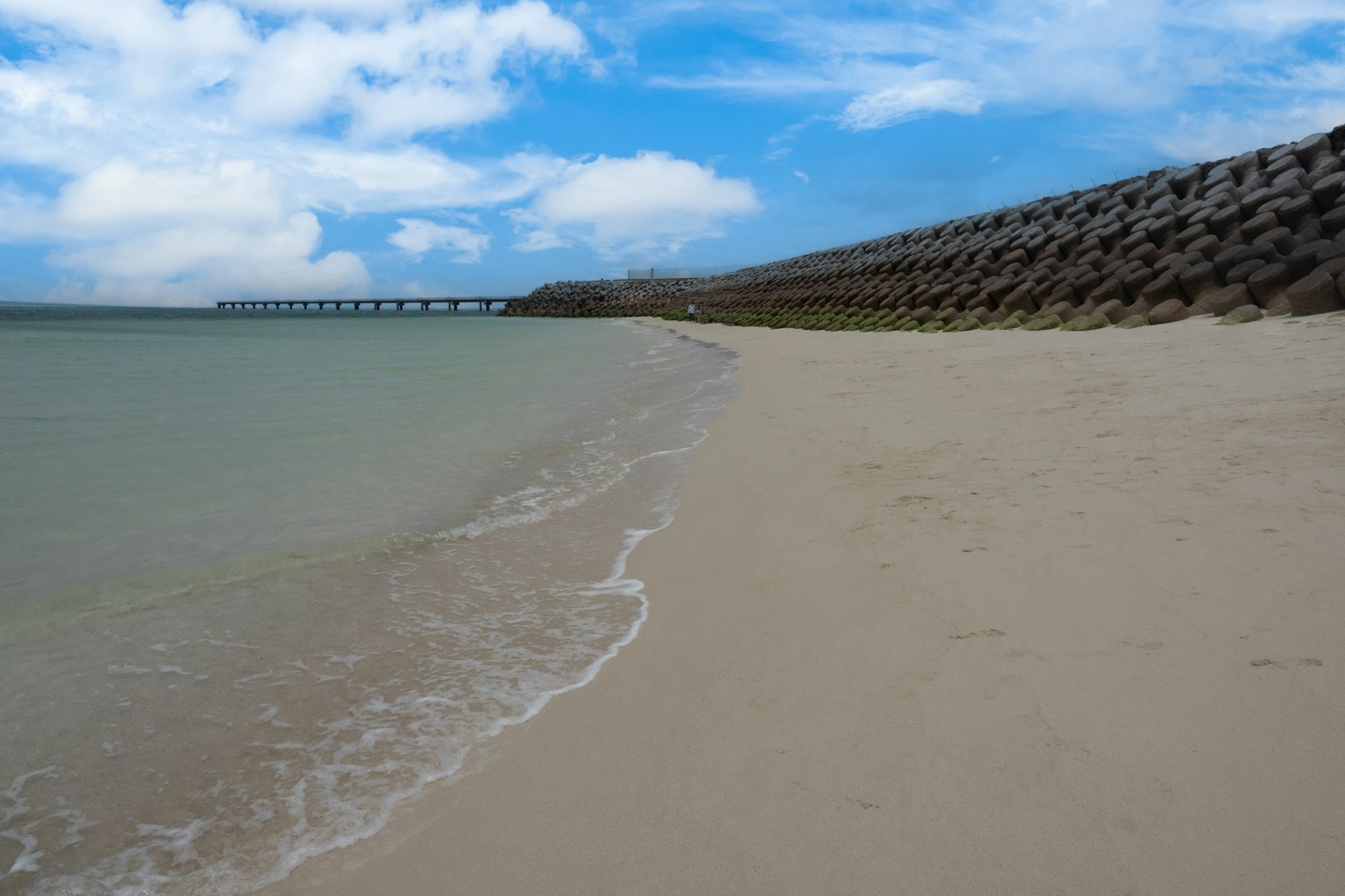 Vue pittoresque de la plage avec ciel bleu et mer calme présentant le rivage sablonneux et un brise-lames
