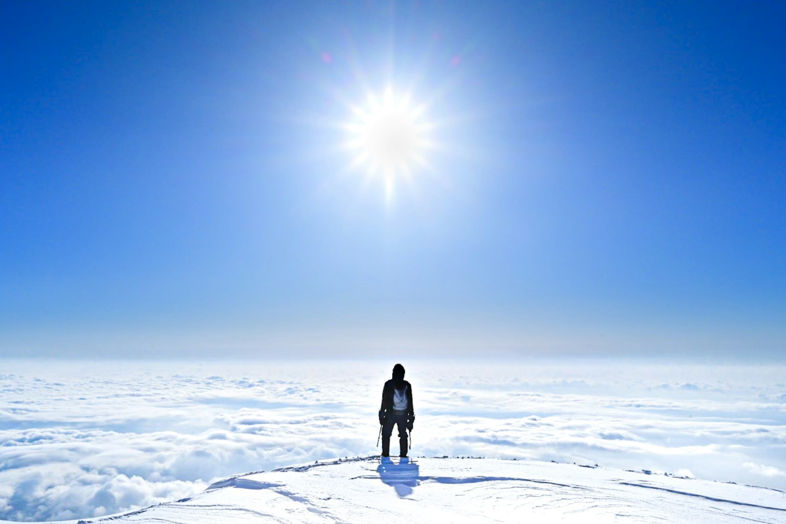 Person standing on snow with bright sun and clear blue sky