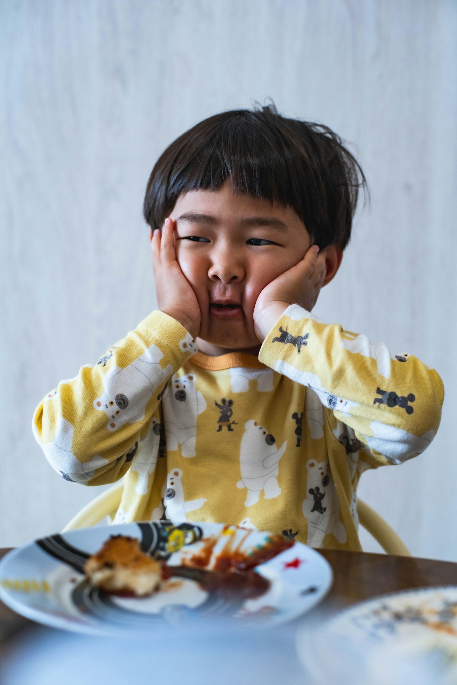 一个坐在桌子旁的孩子双手托着脸穿着黄色睡衣