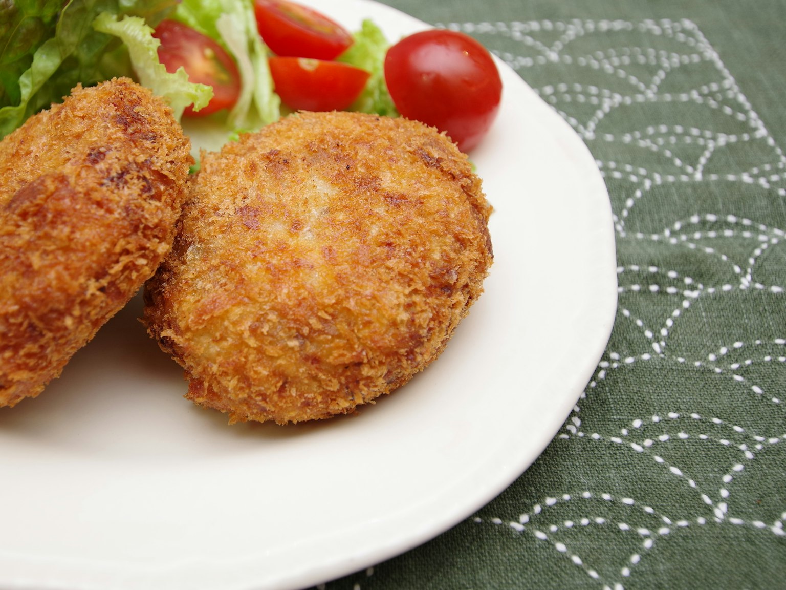 Zwei knusprige Kroketten serviert mit Salat und Kirschtomaten