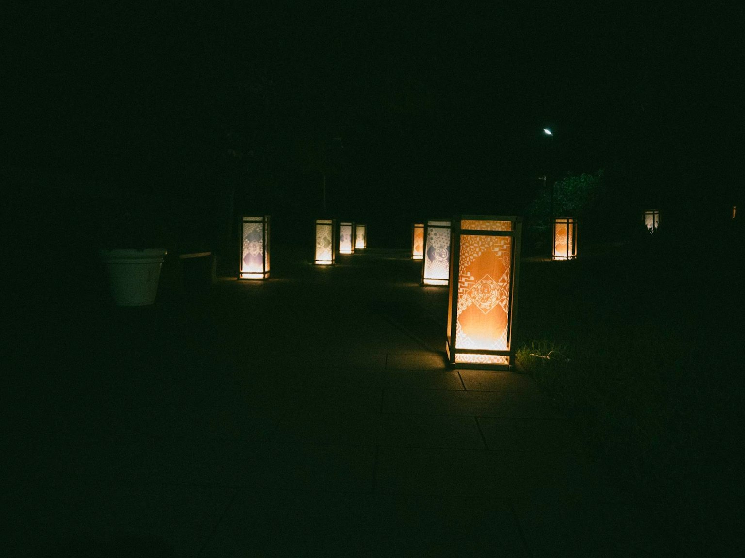 Group of illuminated lanterns along a dark pathway