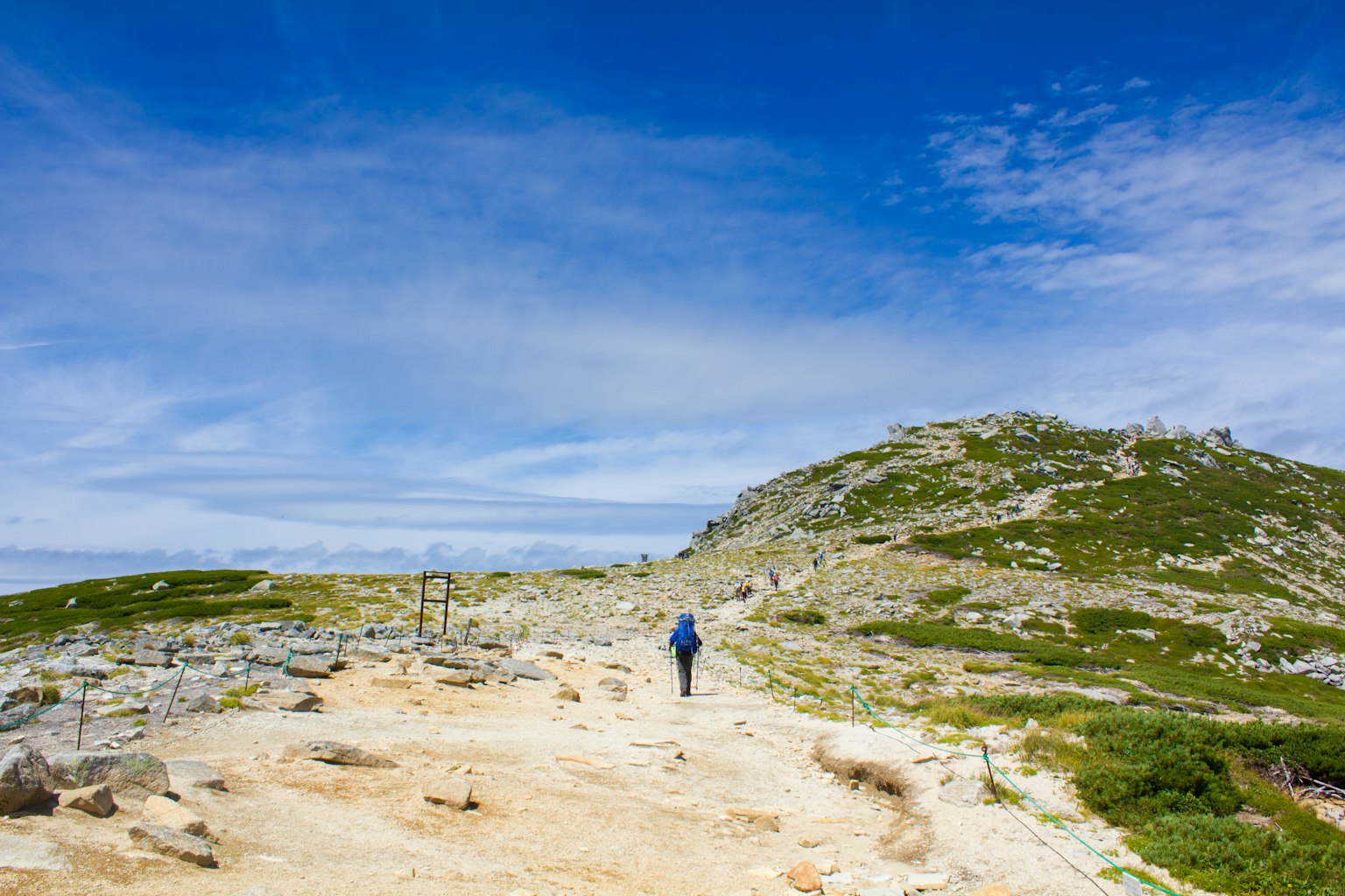 Une personne marchant le long d'un sentier de randonnée sous un ciel bleu et des collines verdoyantes