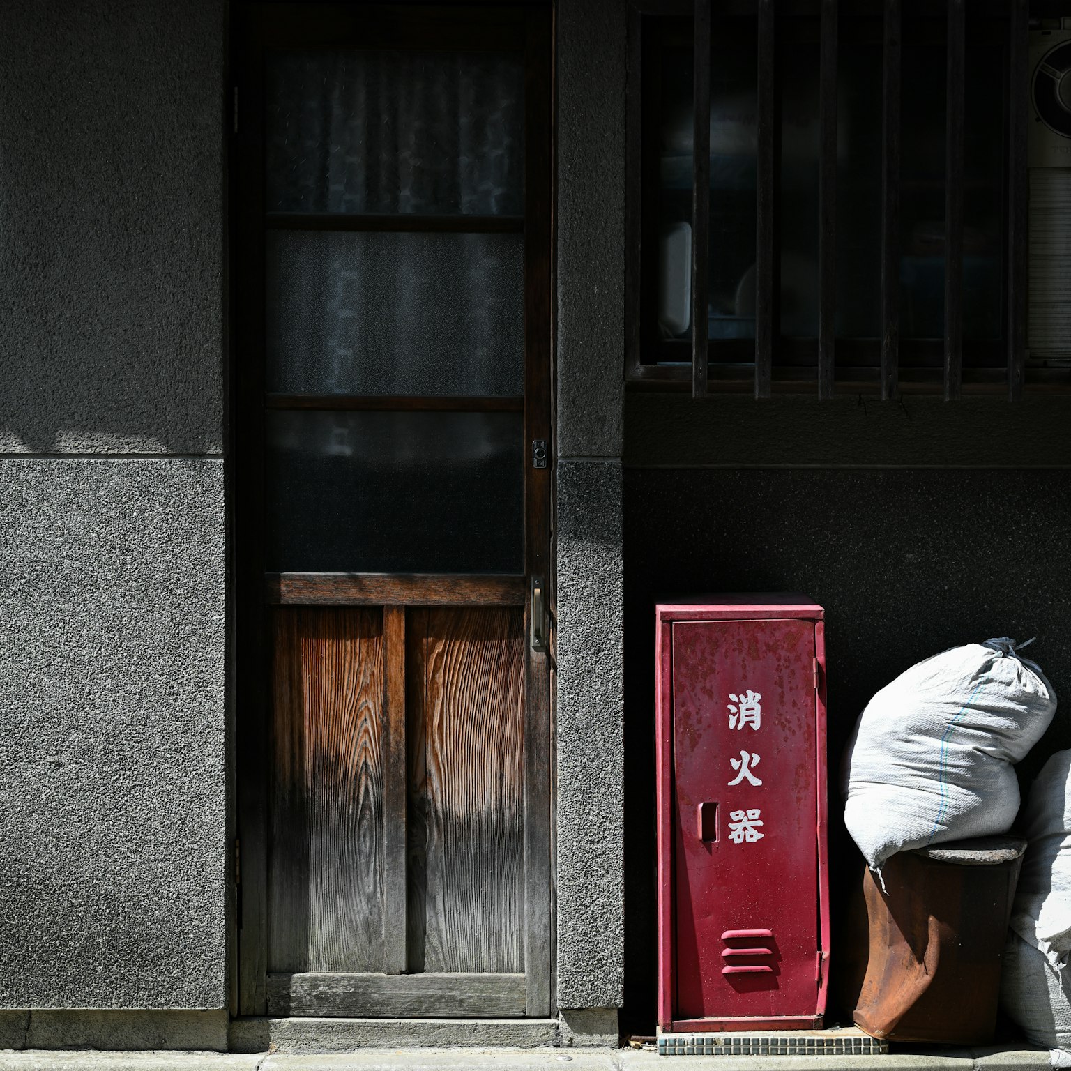 Pintu kayu tua dengan tempat sampah merah di pemandangan jalan Jepang