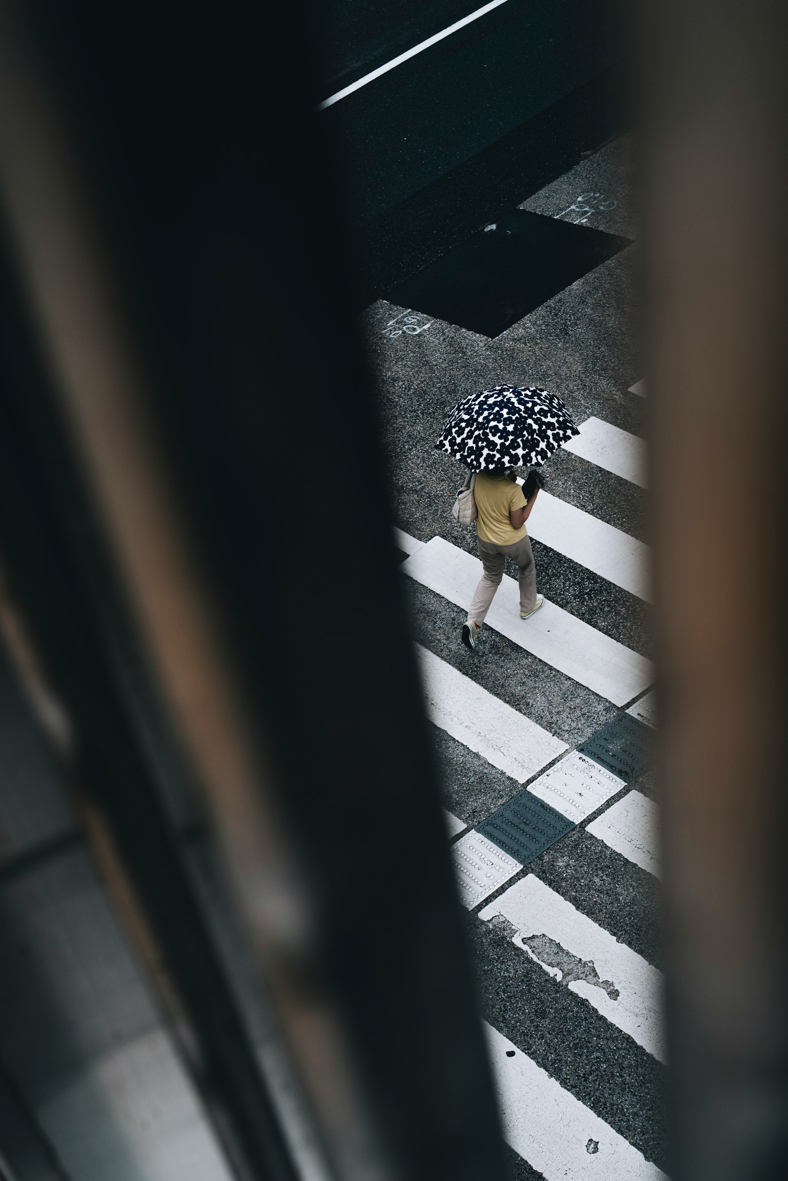 A person with an umbrella walking on a crosswalk from an overhead perspective