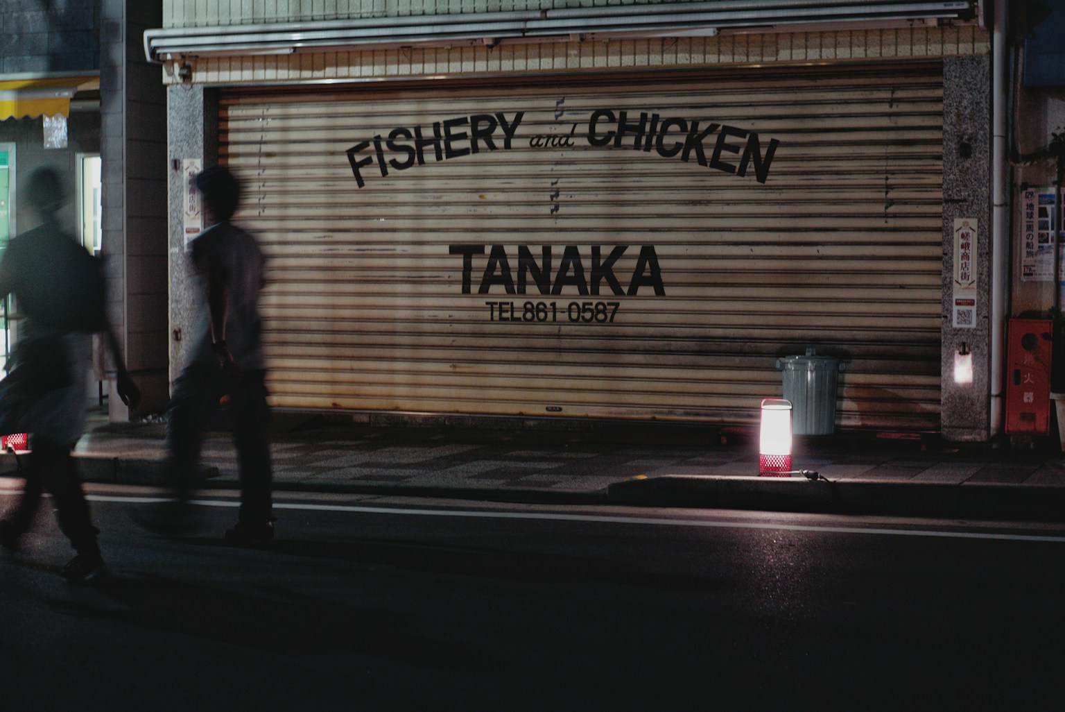 People walking in the night with a sign reading FISHERY CHICKEN TANAKA