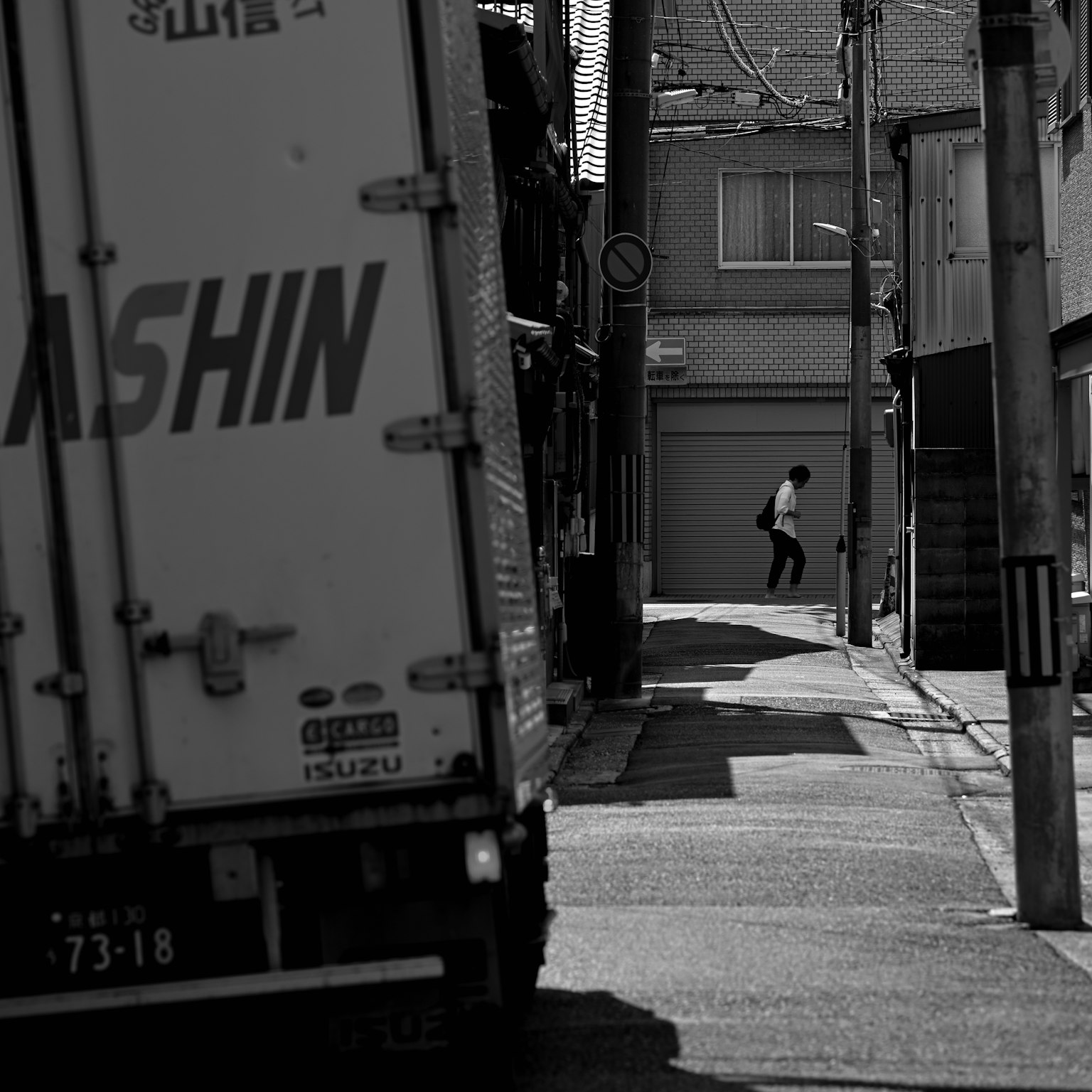 Photo en noir et blanc d'une ruelle étroite avec un camion garé et un piéton