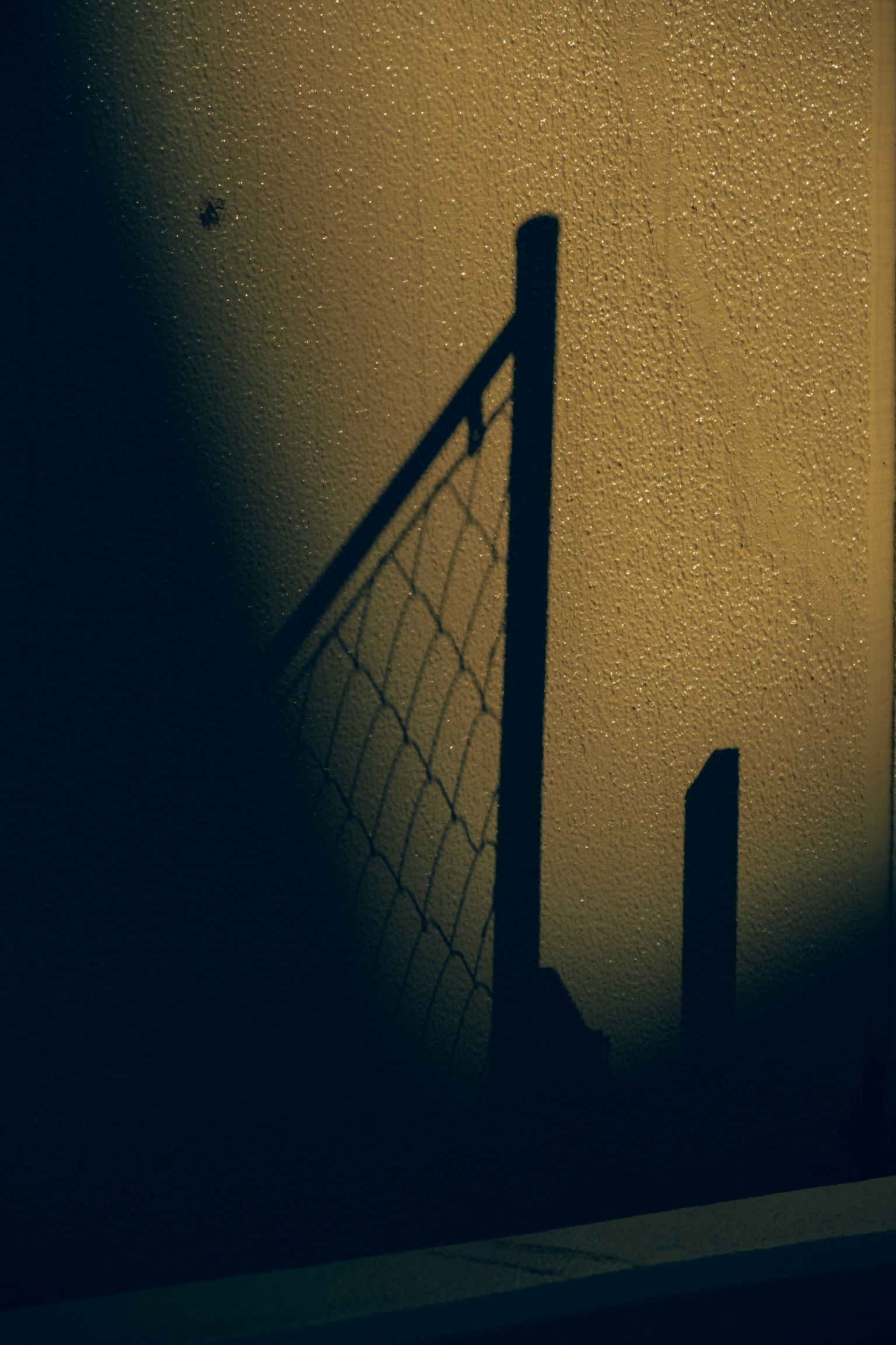 Silhouette eines Zaunschattens an einer strukturierten Wand