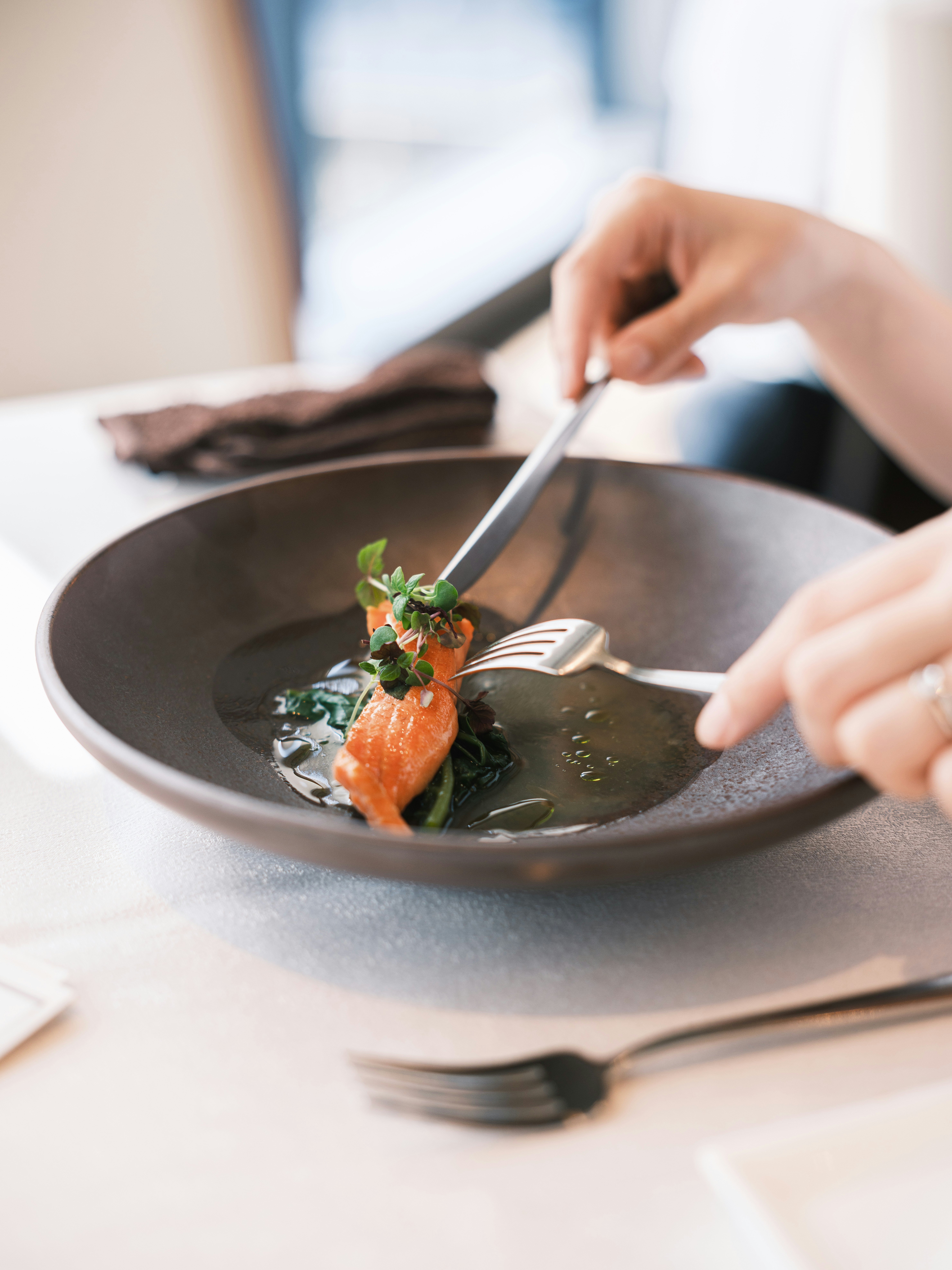 A hand plating a gourmet dish in a bowl with a spoon