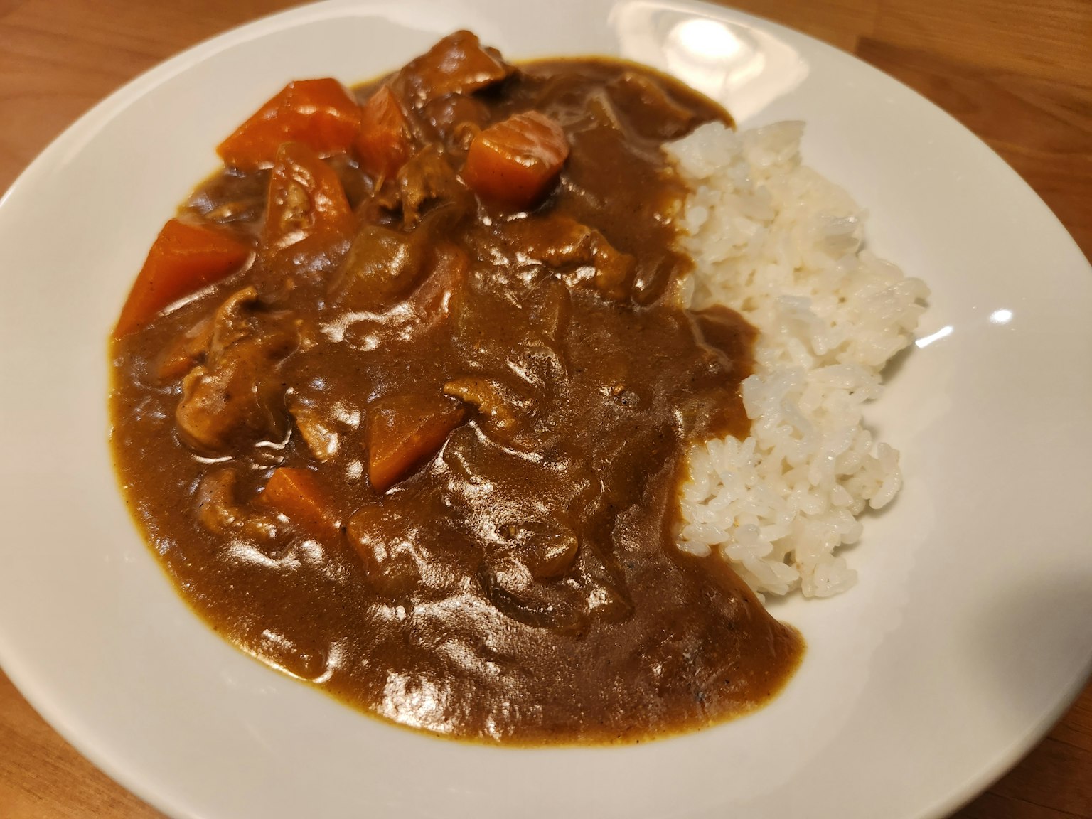 Arroz al curry japonés servido en un plato blanco con pollo y zanahorias en una rica salsa de curry marrón junto a arroz blanco esponjoso