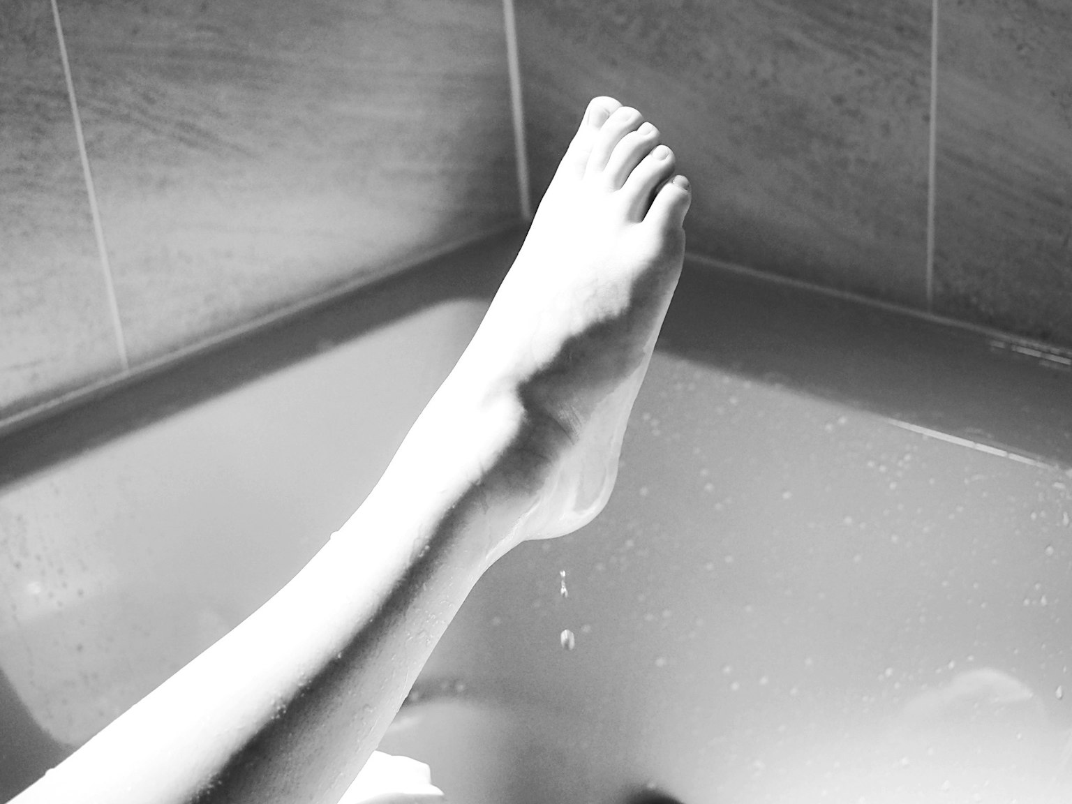 黑白圖像，腳 resting在浴缸邊緣