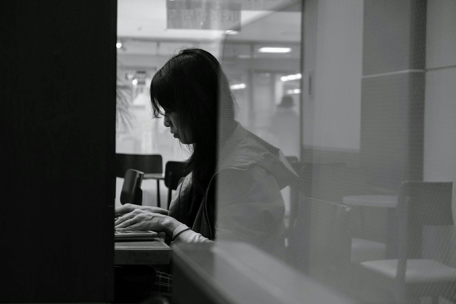 Foto en blanco y negro de una mujer sentada junto a una ventana usando una computadora portátil