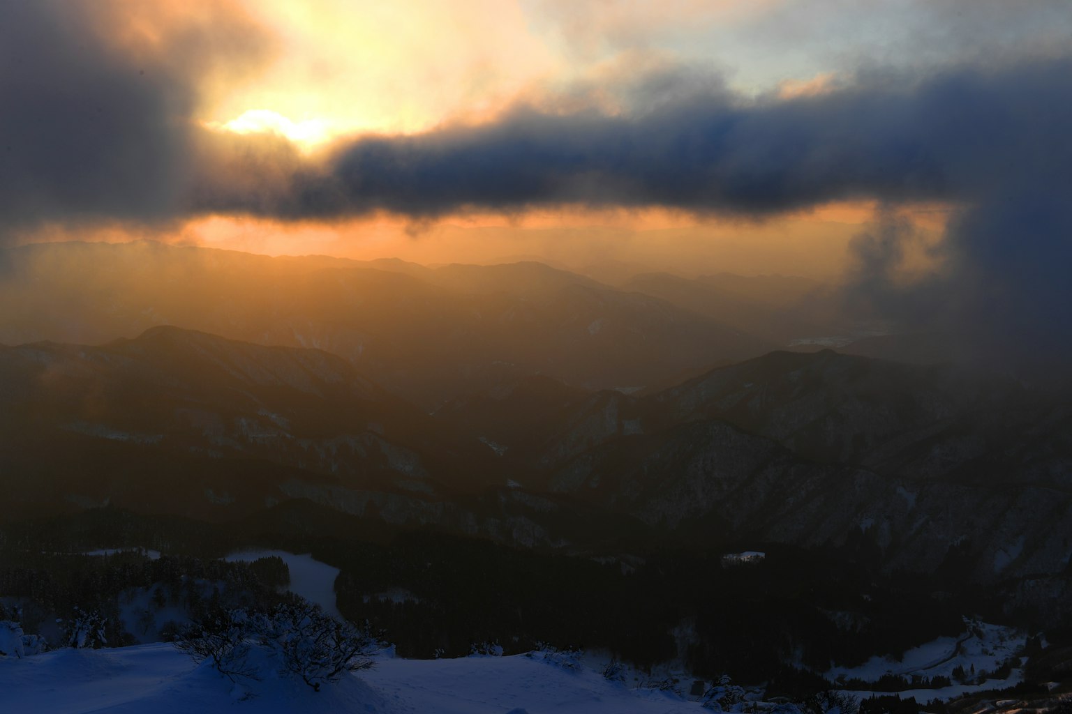 Vista del tramonto da una cima montuosa con nuvole e colline in silhouette