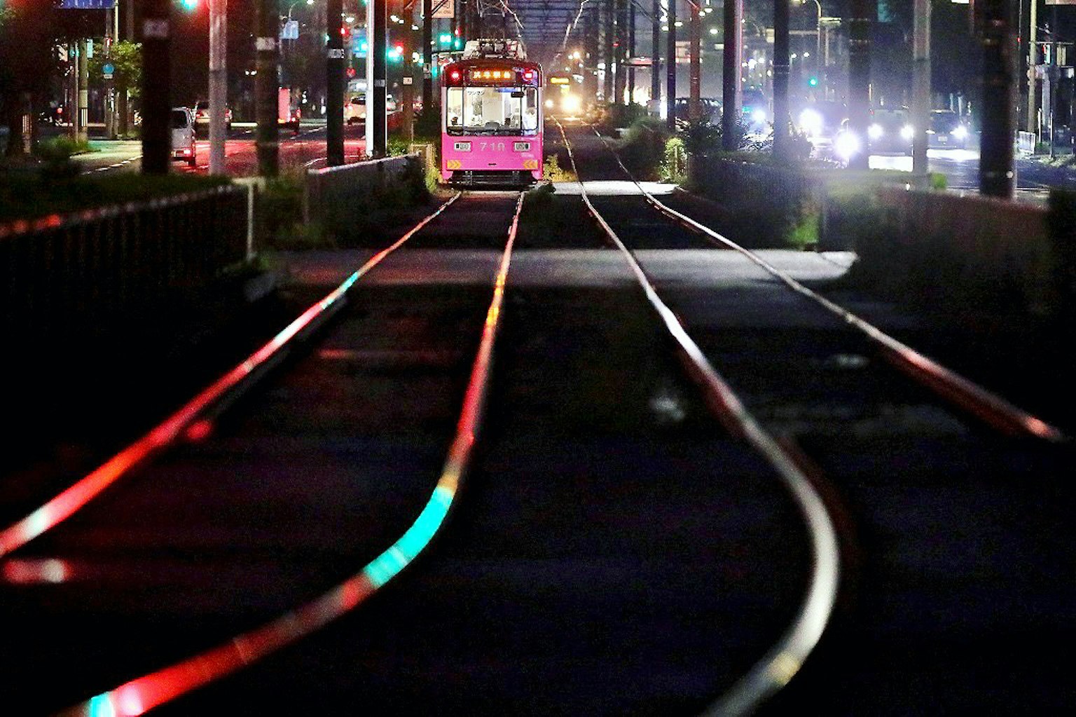 Tram rosa che corre nella città di notte con binari colorati