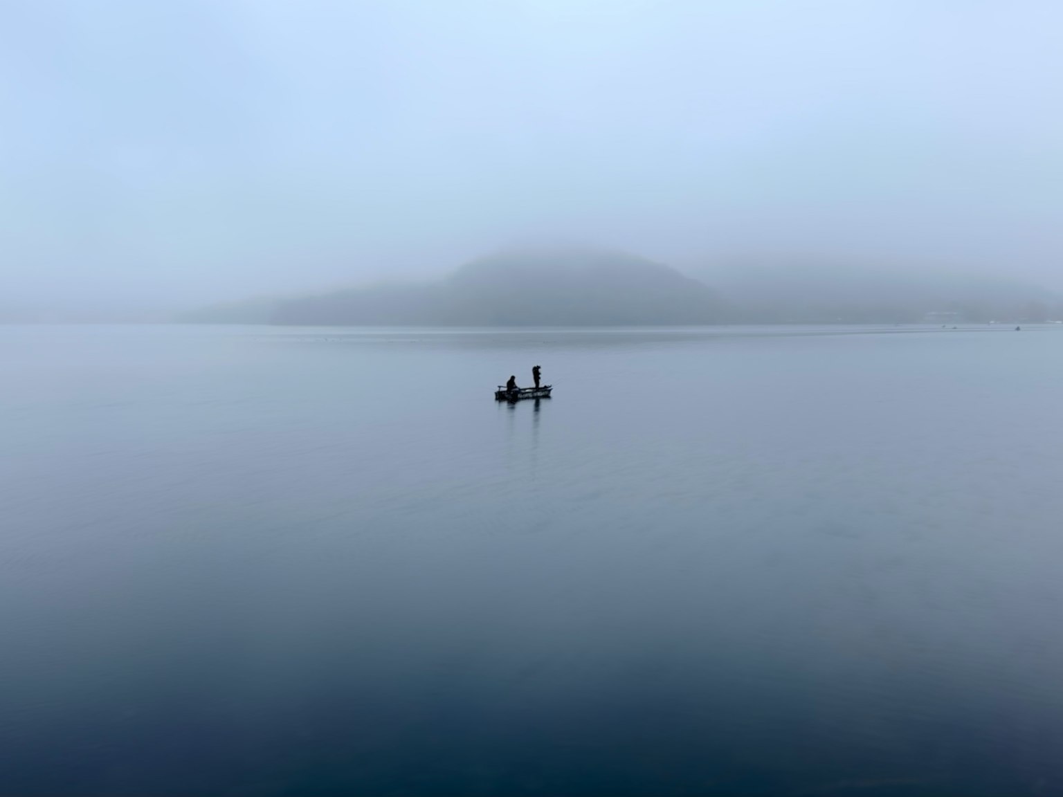 Zwei Fischer in einem Boot auf einem ruhigen See umgeben von Nebel