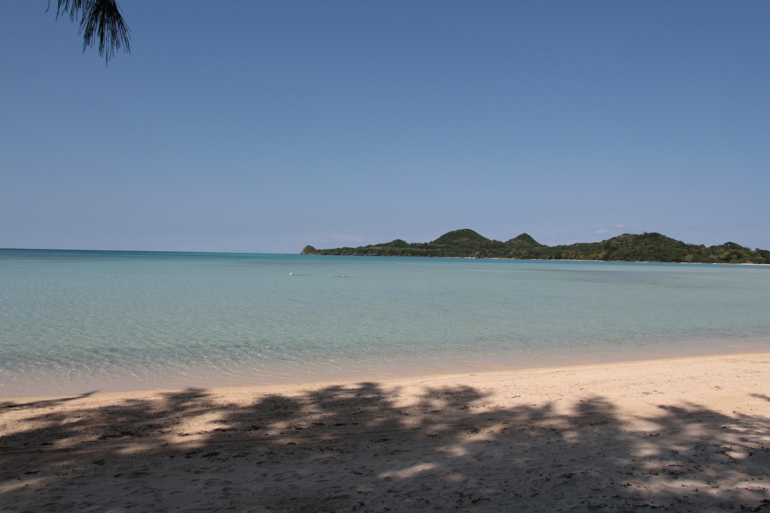 ทิวทัศน์ชายหาดที่เงียบสงบพร้อมน้ำสีฟ้าและเกาะที่อยู่ไกล