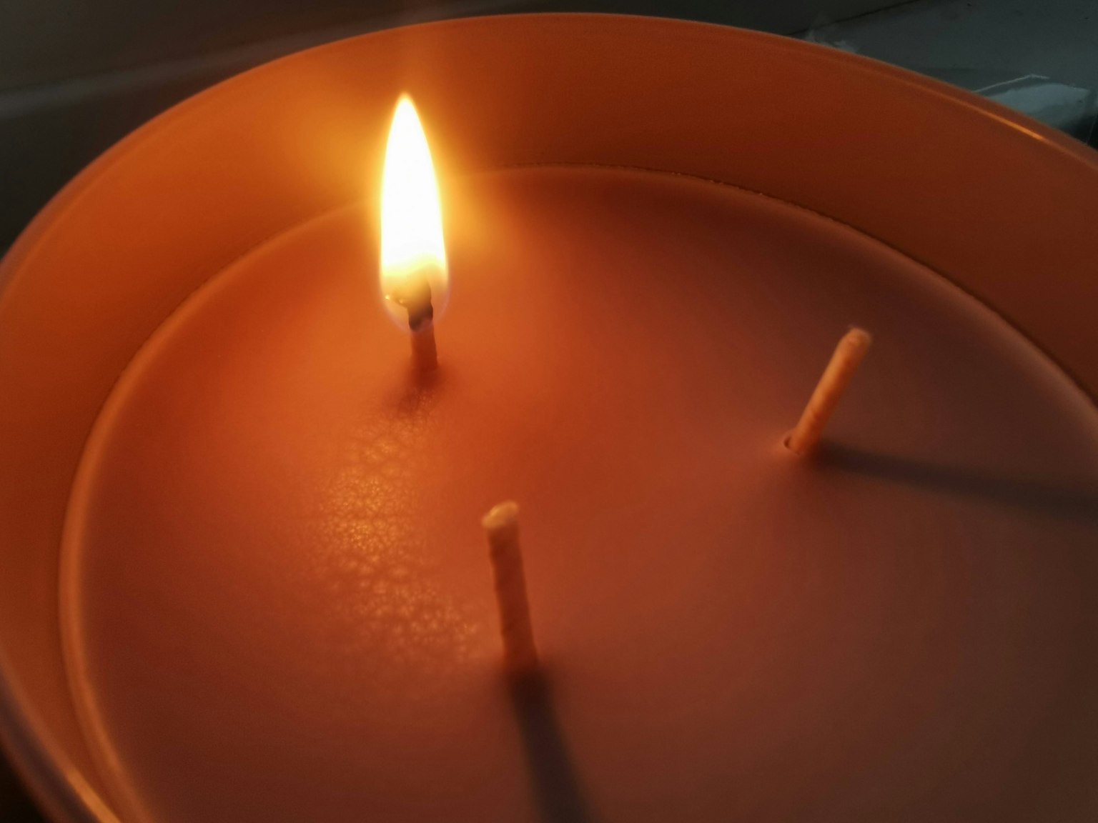 Orange candle with a lit wick and two unlit wicks