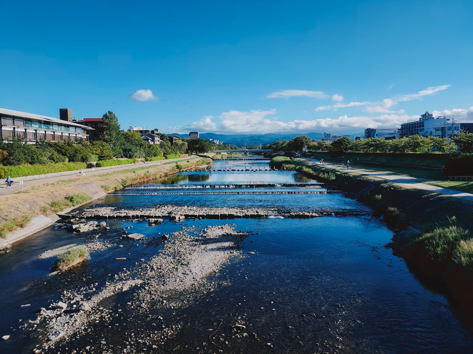 青空と山々が背景の川の風景 流れる水と石の橋が特徴