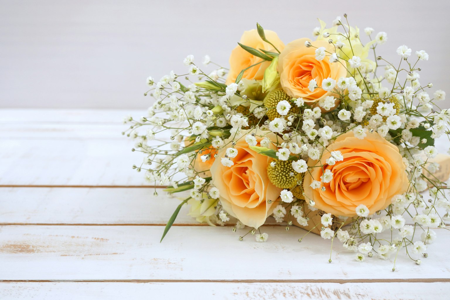 Ein Strauß aus blassorangefarbenen Rosen und Schleierkraut auf einem weißen Holzuntergrund