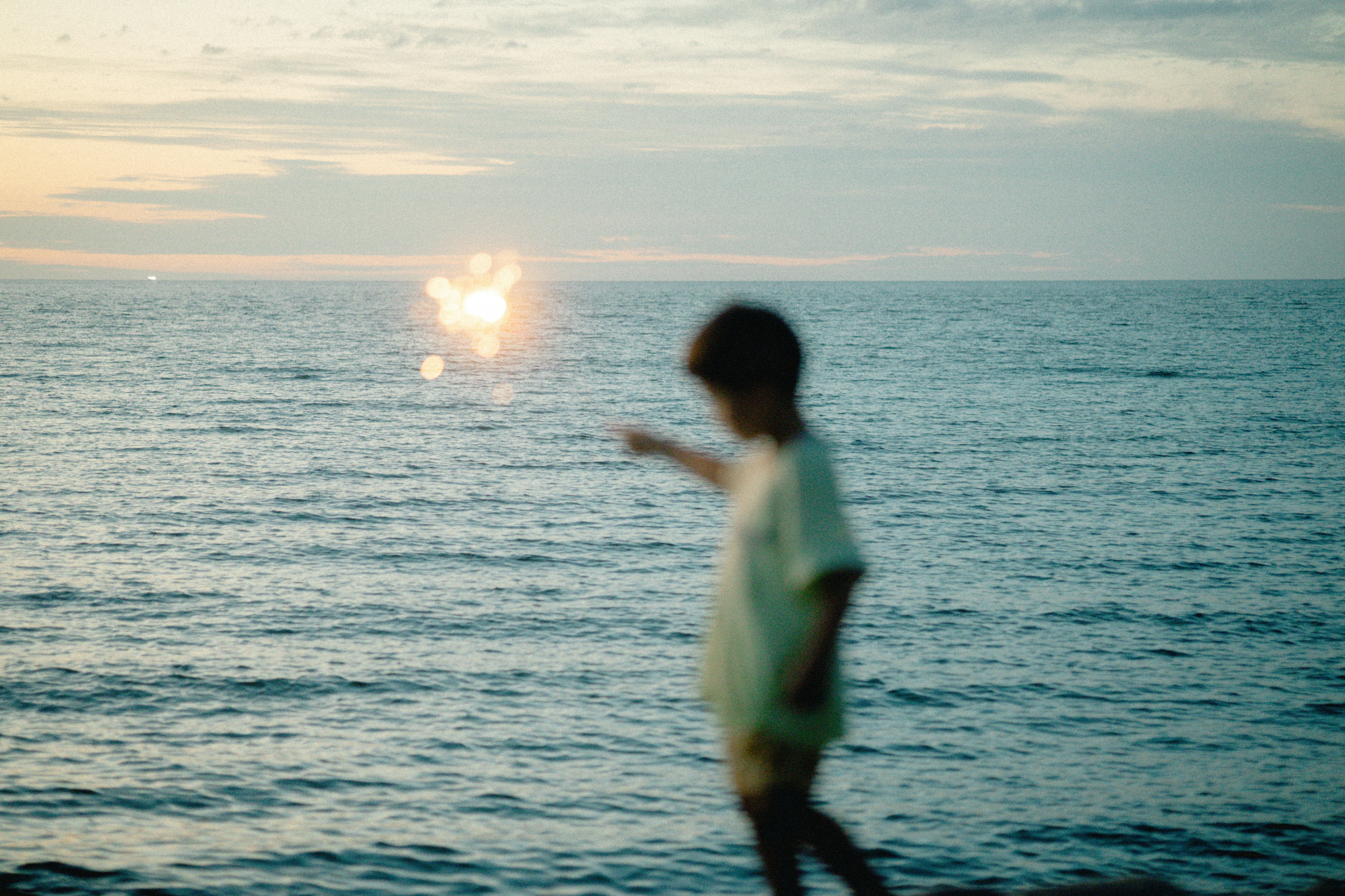 Silhouette of a child playing by the seaside against a sunset backdrop