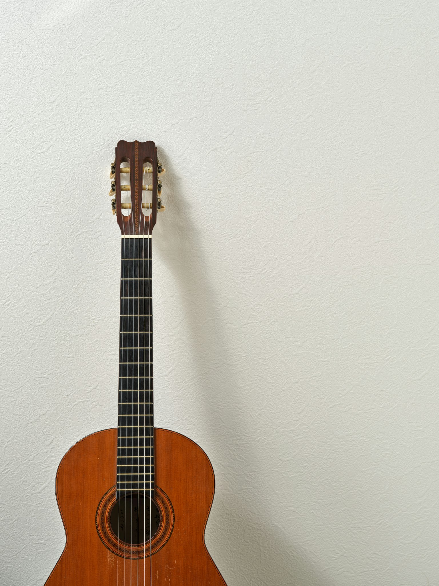 Una guitarra clásica marrón apoyada contra una pared blanca