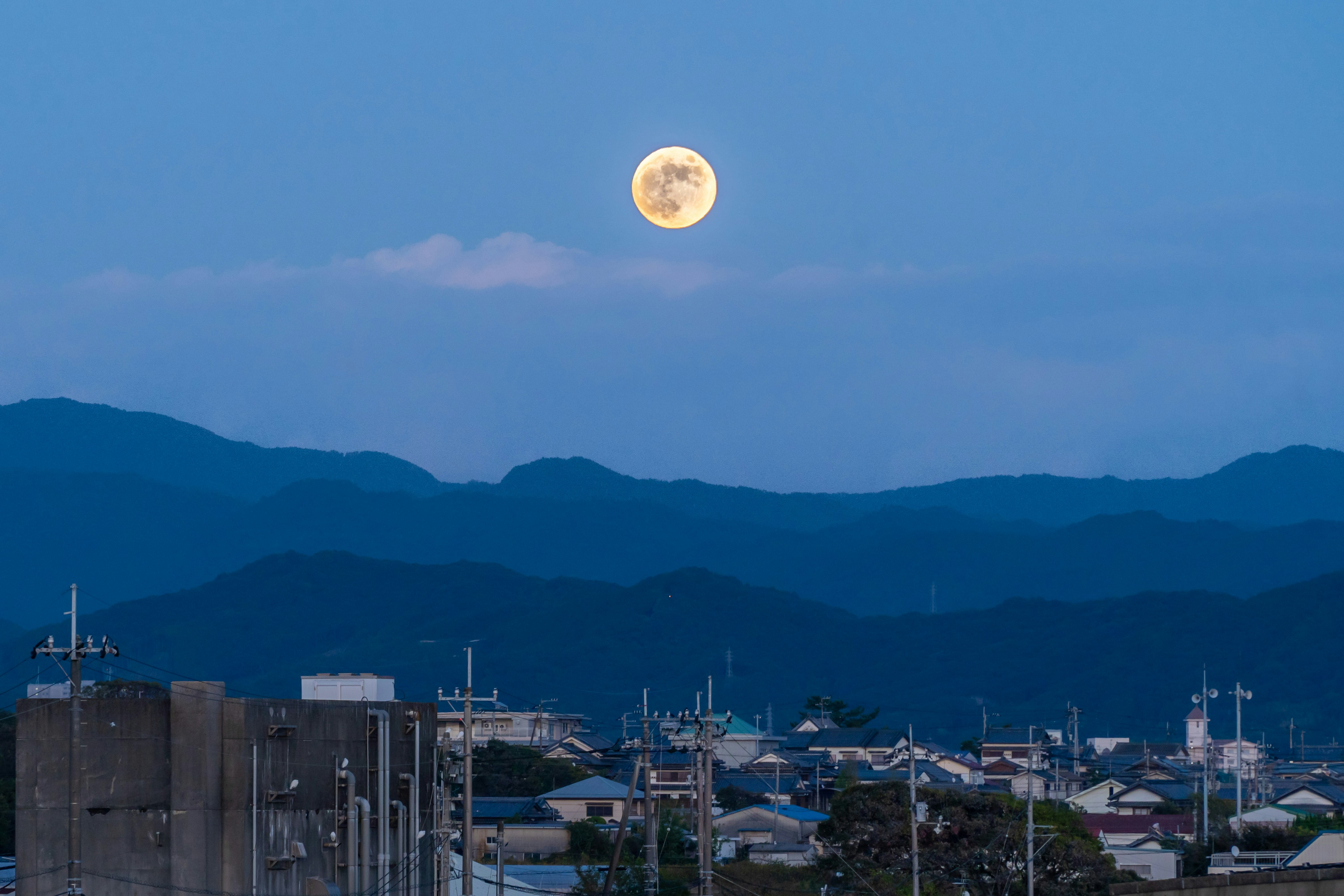 工場群と山並みを望む夕暮れの空に浮かぶ月