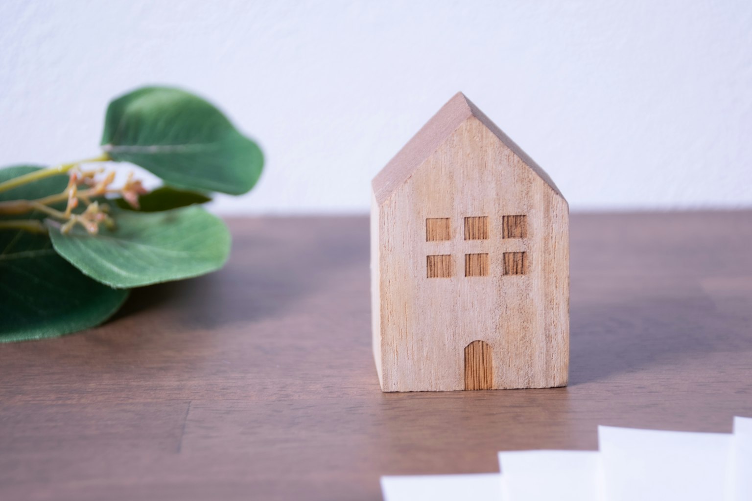 Ein Holzmodell eines Hauses auf einem Tisch mit grünen Blättern in der Nähe