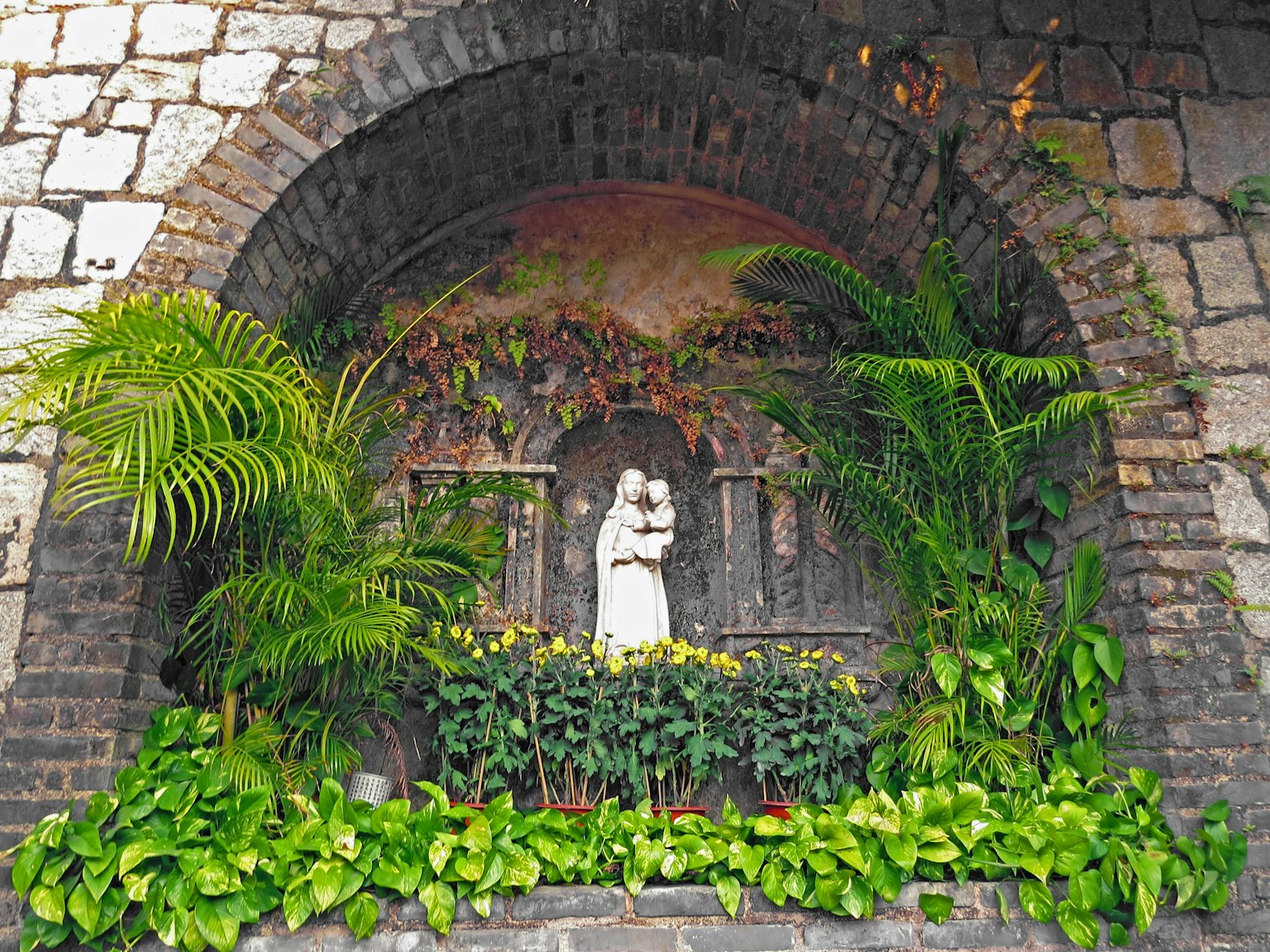 Archway niche featuring a statue of the Virgin Mary surrounded by lush greenery