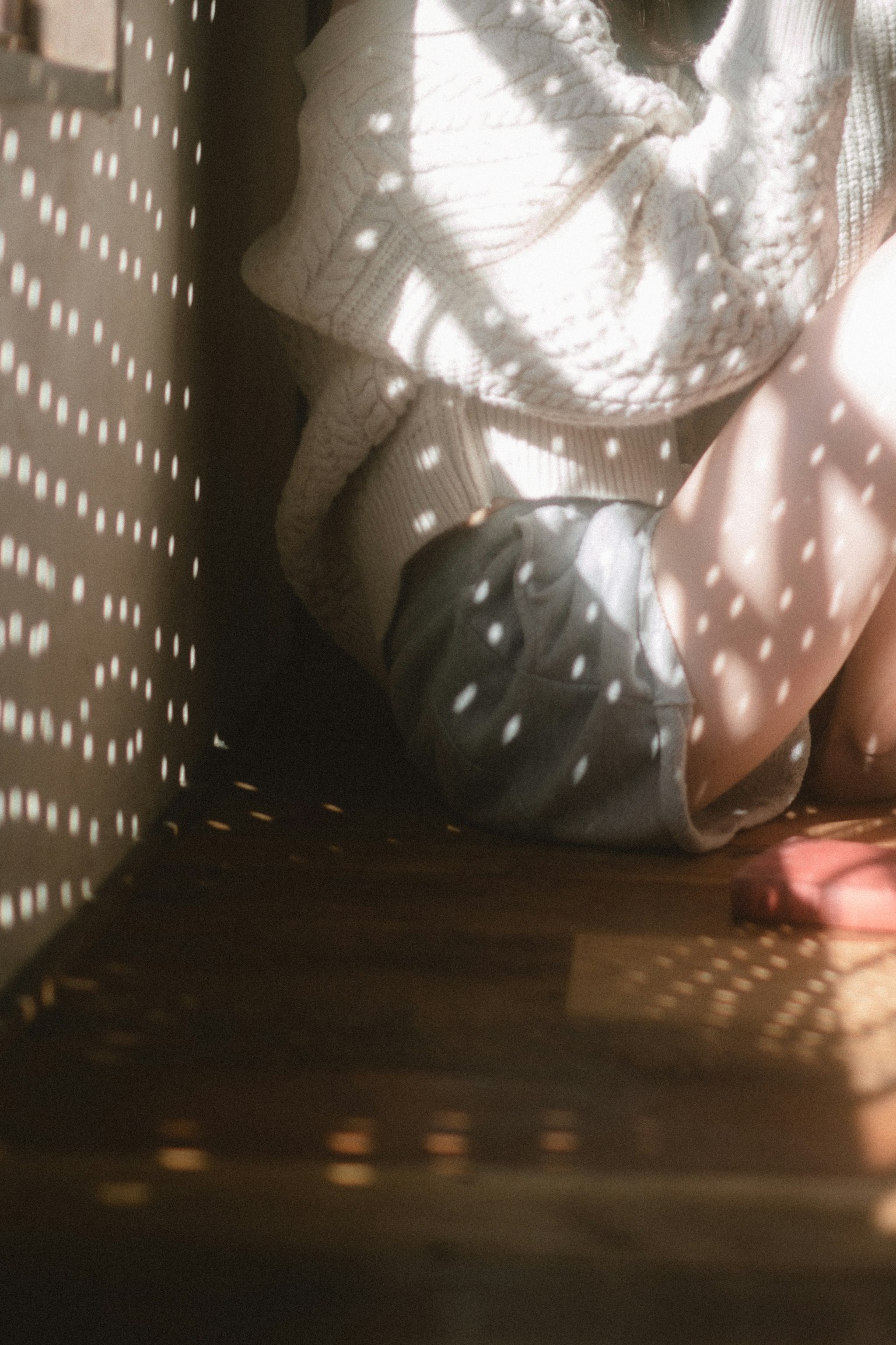 A person sitting in a corner of a room with soft light creating shadows