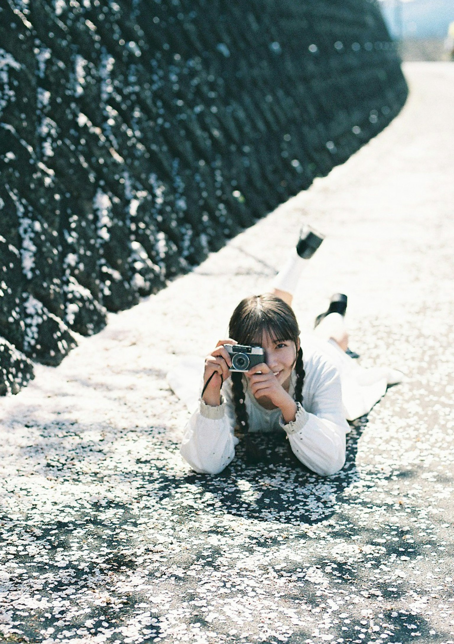 Ragazza sdraiata vicino all'acqua con una macchina fotografica indossando abiti bianchi e scarpe nere riflessi sulla superficie dell'acqua