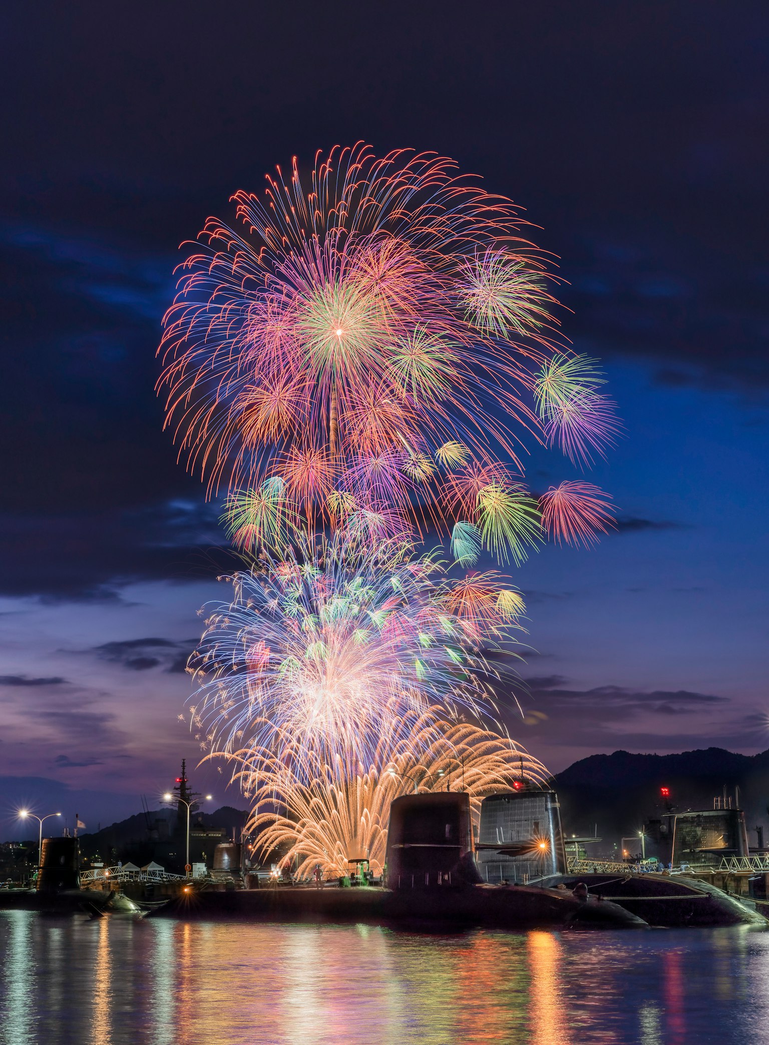 Fuochi d'artificio colorati esplodono nel cielo notturno riflettendosi sull'acqua