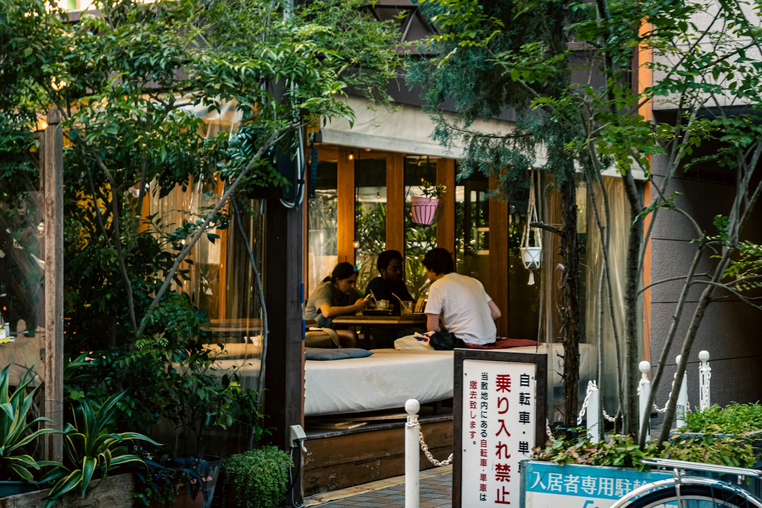 Außenansicht eines Cafés, umgeben von Grün, mit Gästen an einem Tisch