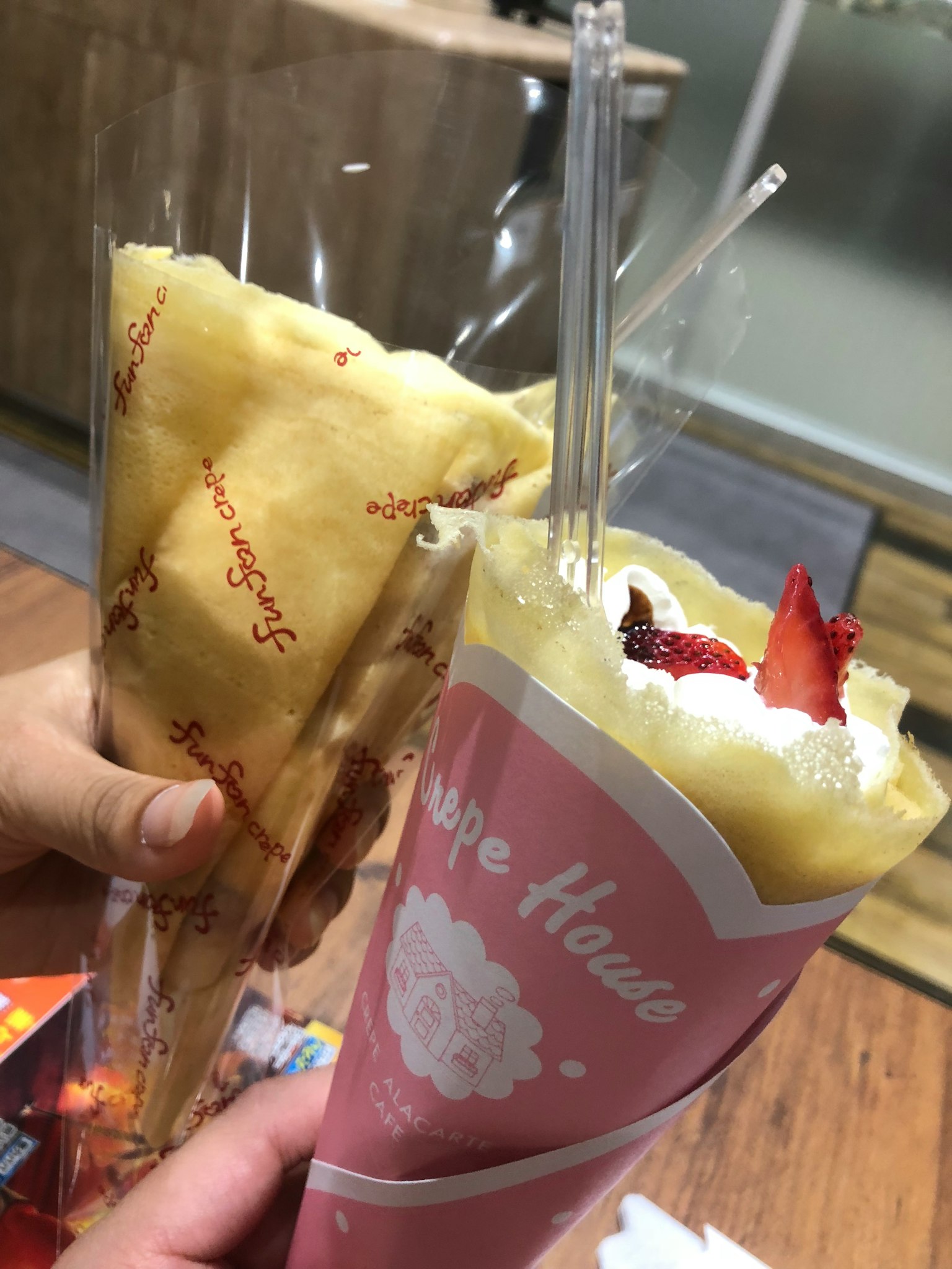 Due crêpes tenute in mano Una ha una copertura di crema di fragole in un involucro rosa L'altra è un involucro giallo semplice ripieno di crema