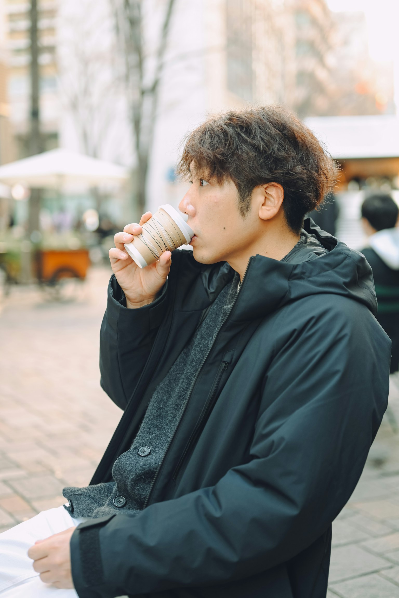 在咖啡馆喝饮料的男性，穿着黑色外套，城市背景