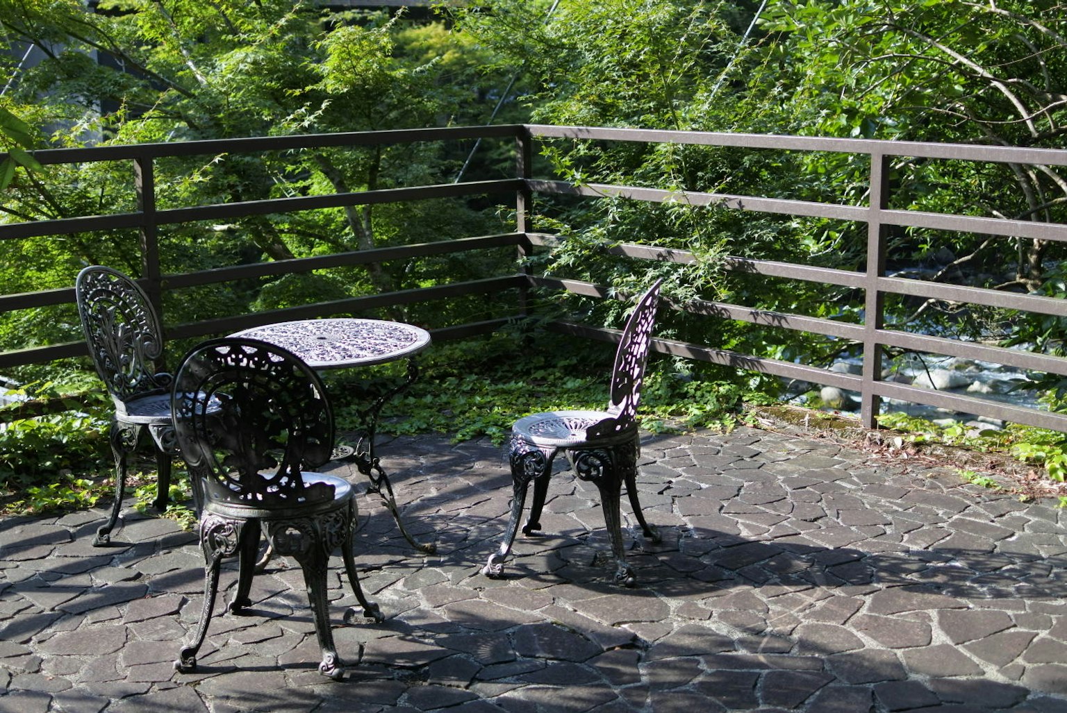 Eisen-Tisch- und Stuhlset auf einer Terrasse, umgeben von Grün