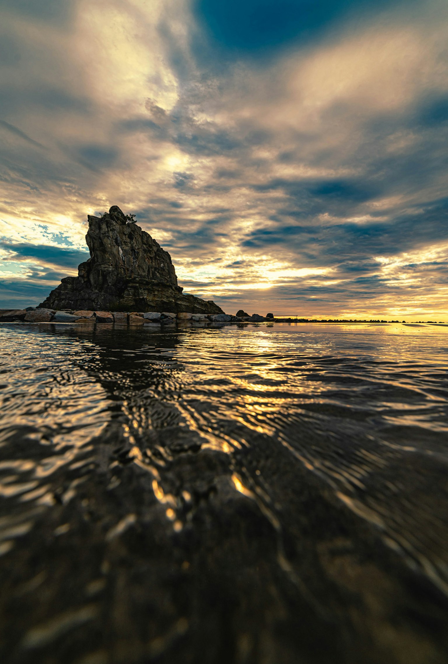 Paysage d'un rocher dans la mer reflétant le ciel du coucher de soleil
