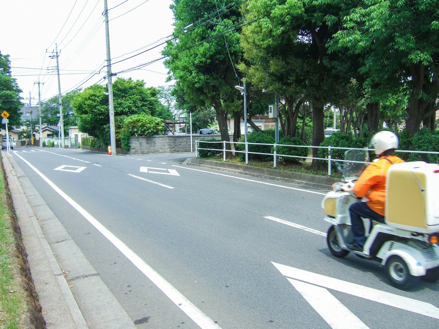 A delivery person in an orange uniform riding a scooter on a street