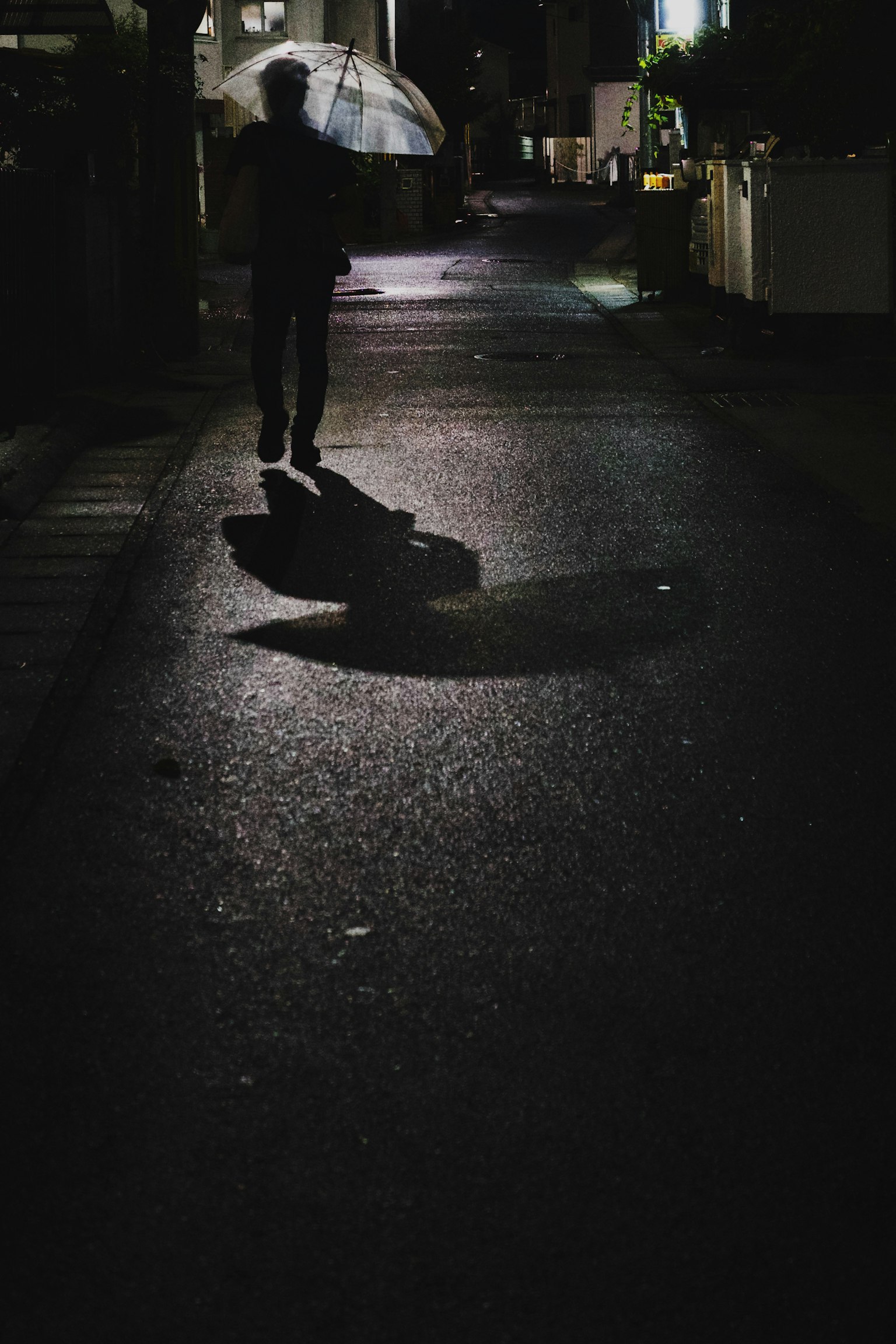 Silhouette of a person walking in a dark alley holding an umbrella with shadows