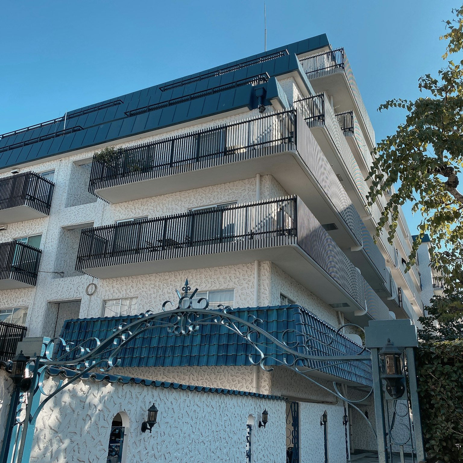 Dreistöckiges Gebäude mit weißer Fassade Balkone und blauer Dachgestaltung